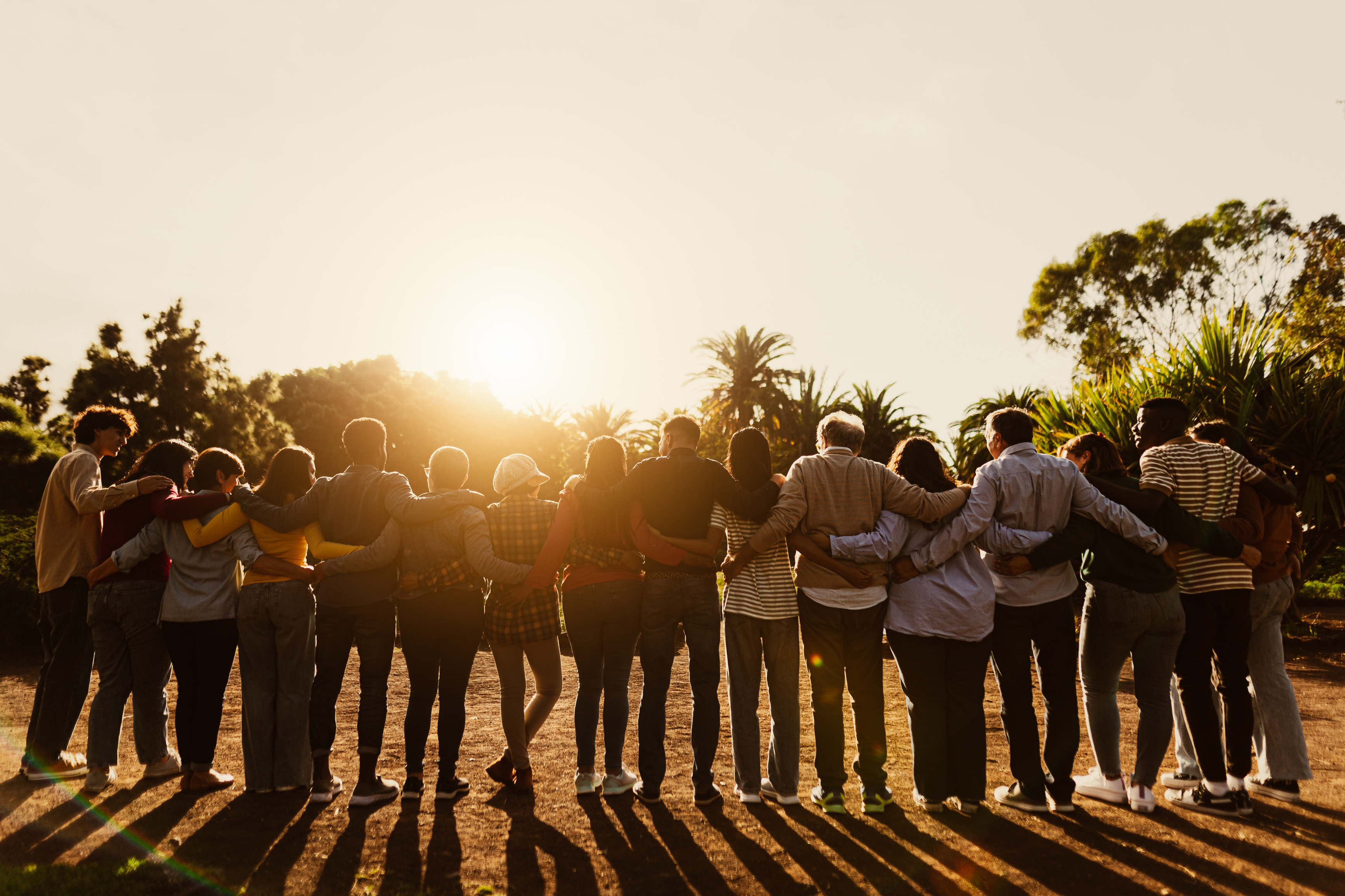 A large group of travellers embrace while watching a sunset 
