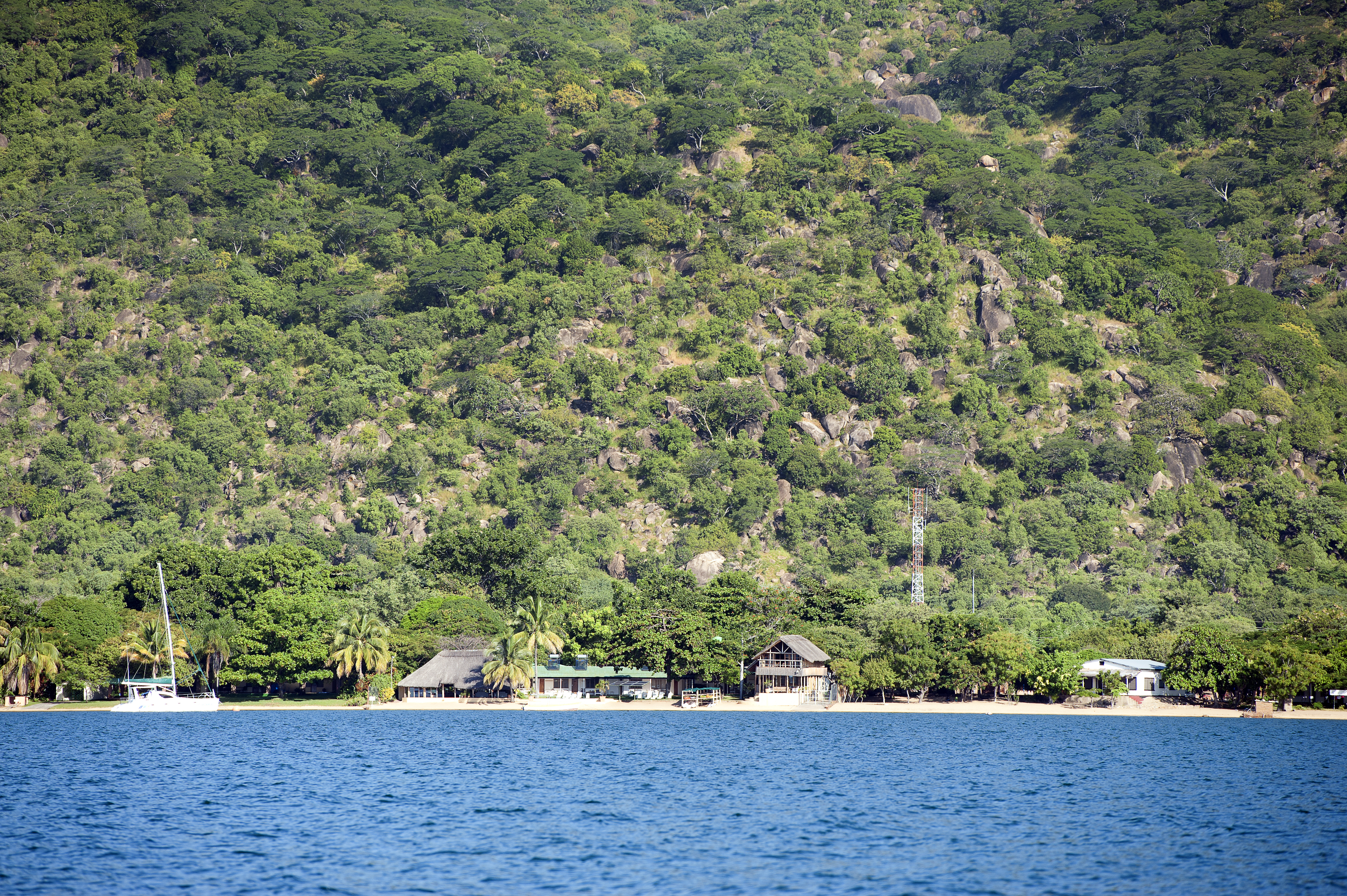 A panoramic view of Lake Malawi, Africa. The lake is surrounded by lush green hills and has crystal-clear blue water.