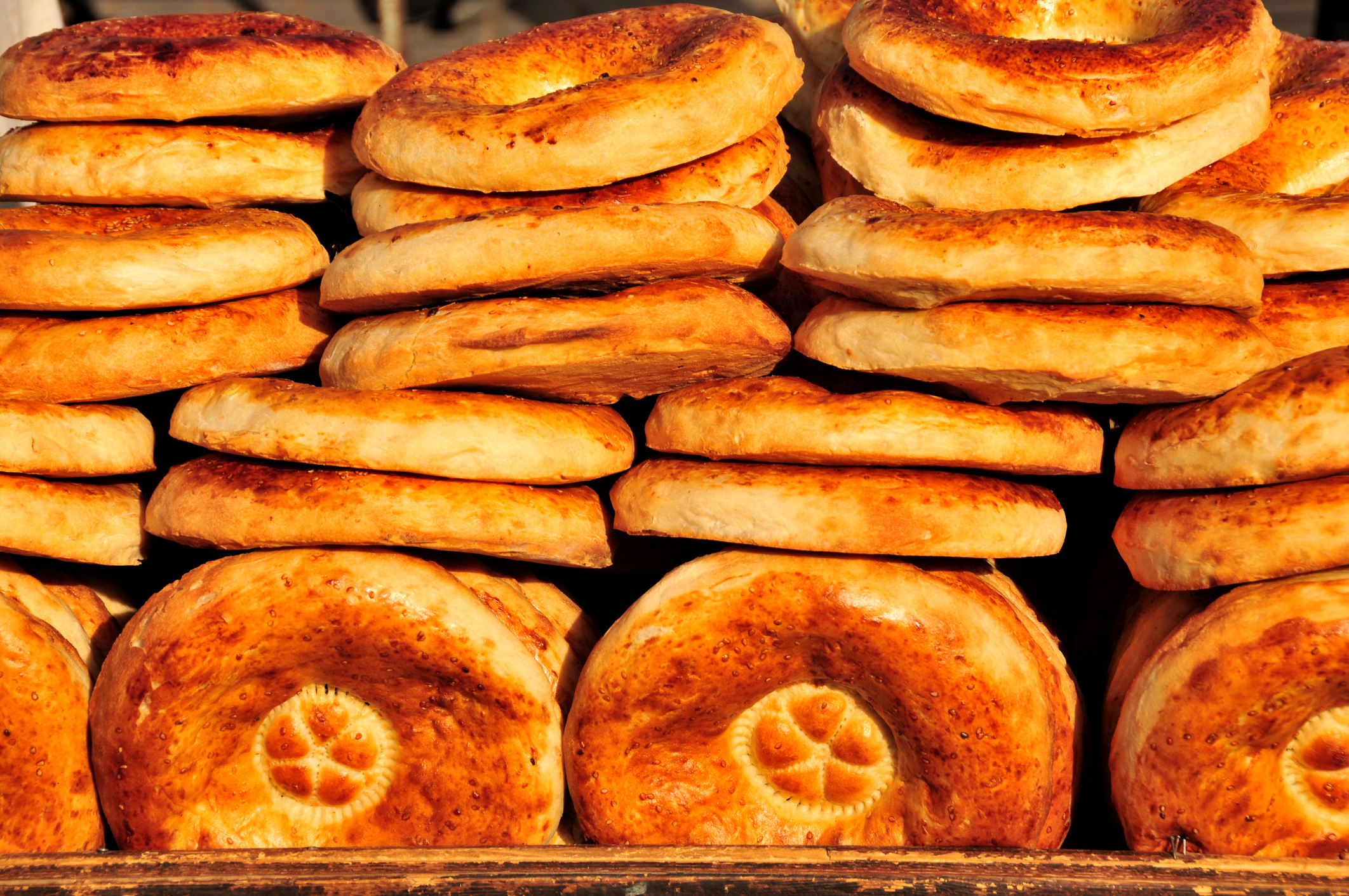 A stack of freshly baked round bread, golden brown with a slightly crisp surface and a decorative pattern on top.