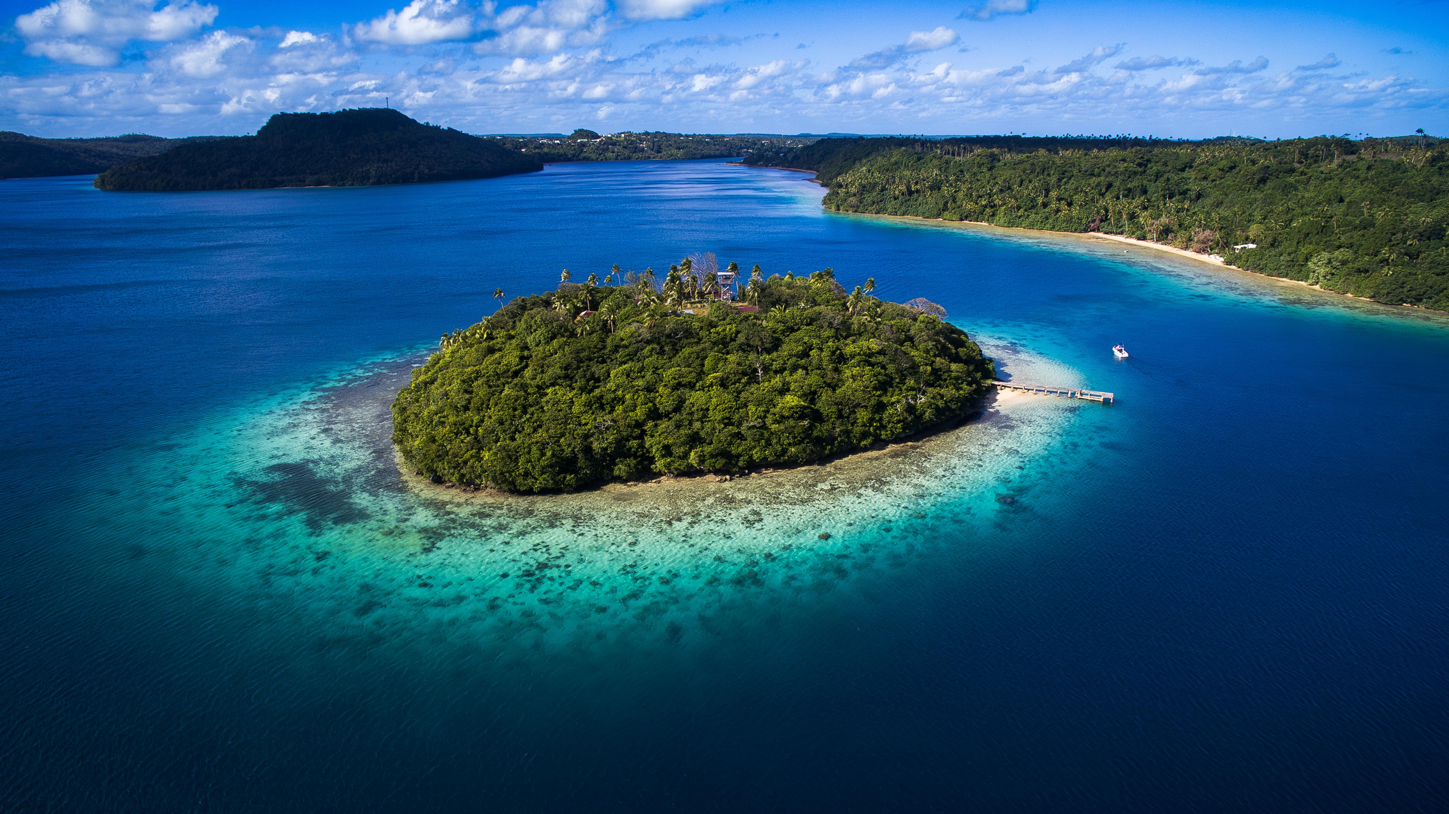 Aerial view of tiny tropical island surrounded by pristine blue water and coral reef in Tonga