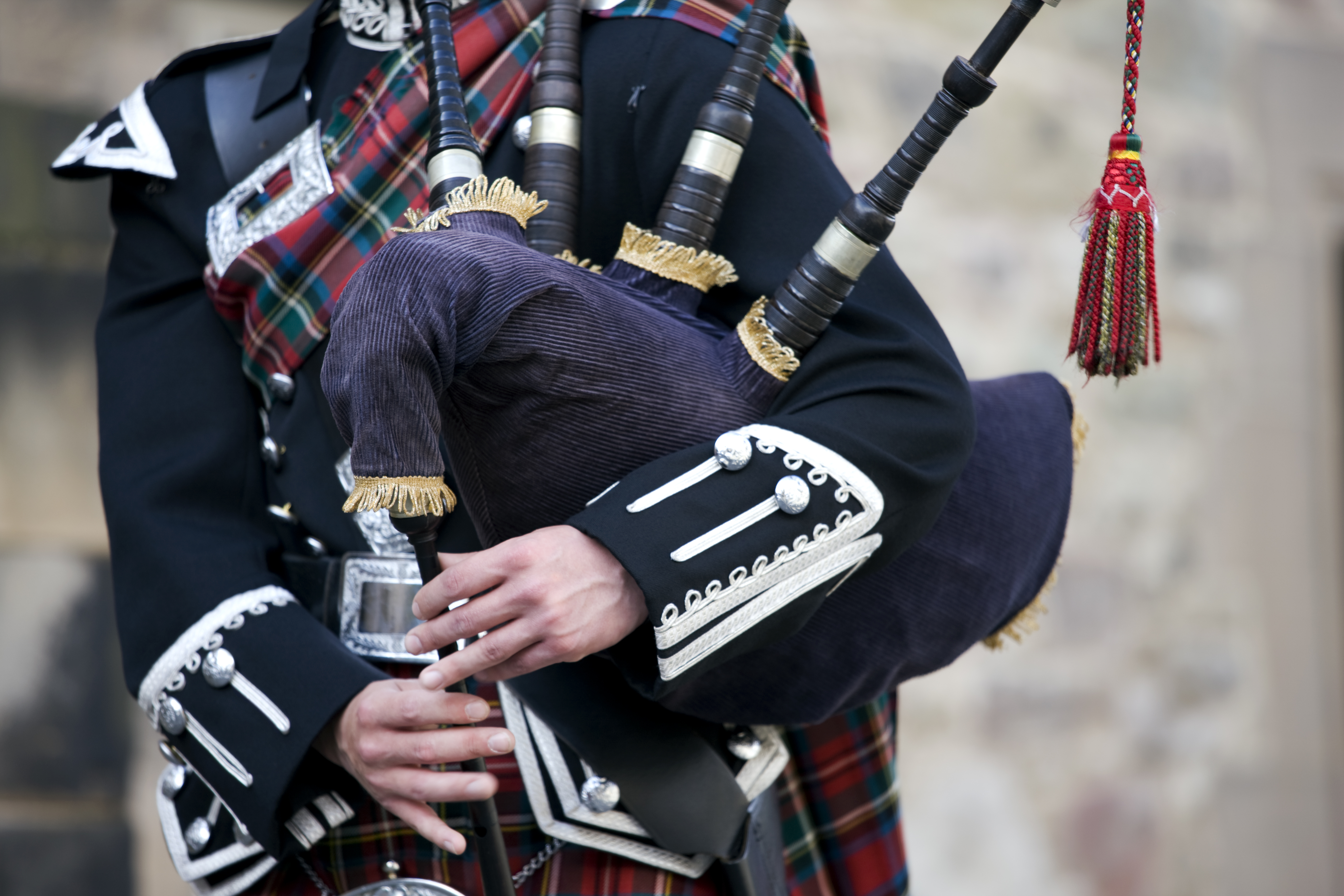 Close up of the hands of a Scottish bagpiper clad in a traditional scottish tartan playing the Scottish bagpipe