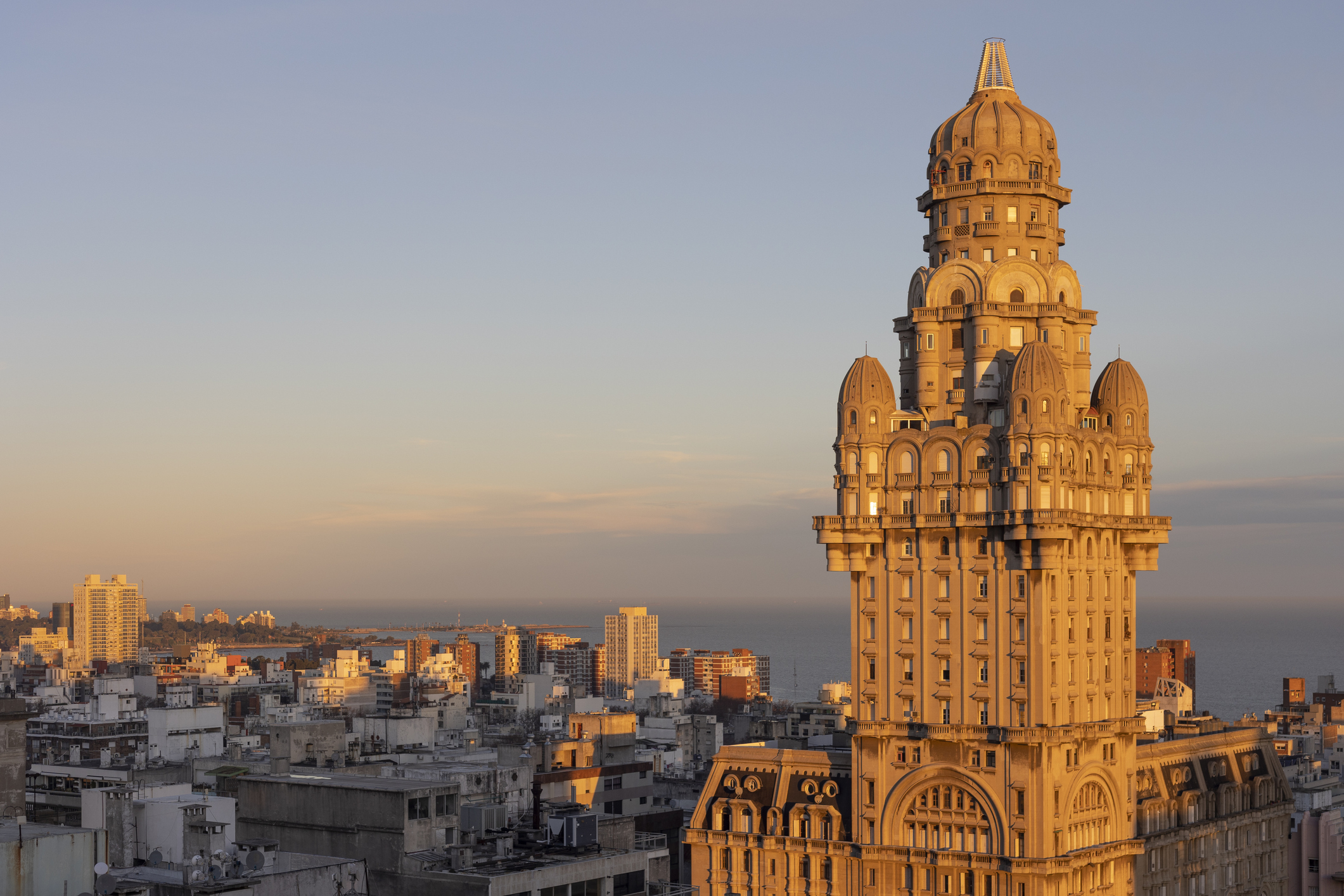 Historic tall building with intricate architecture, bathed in sunset light, overlooking a city skyline and coastline.