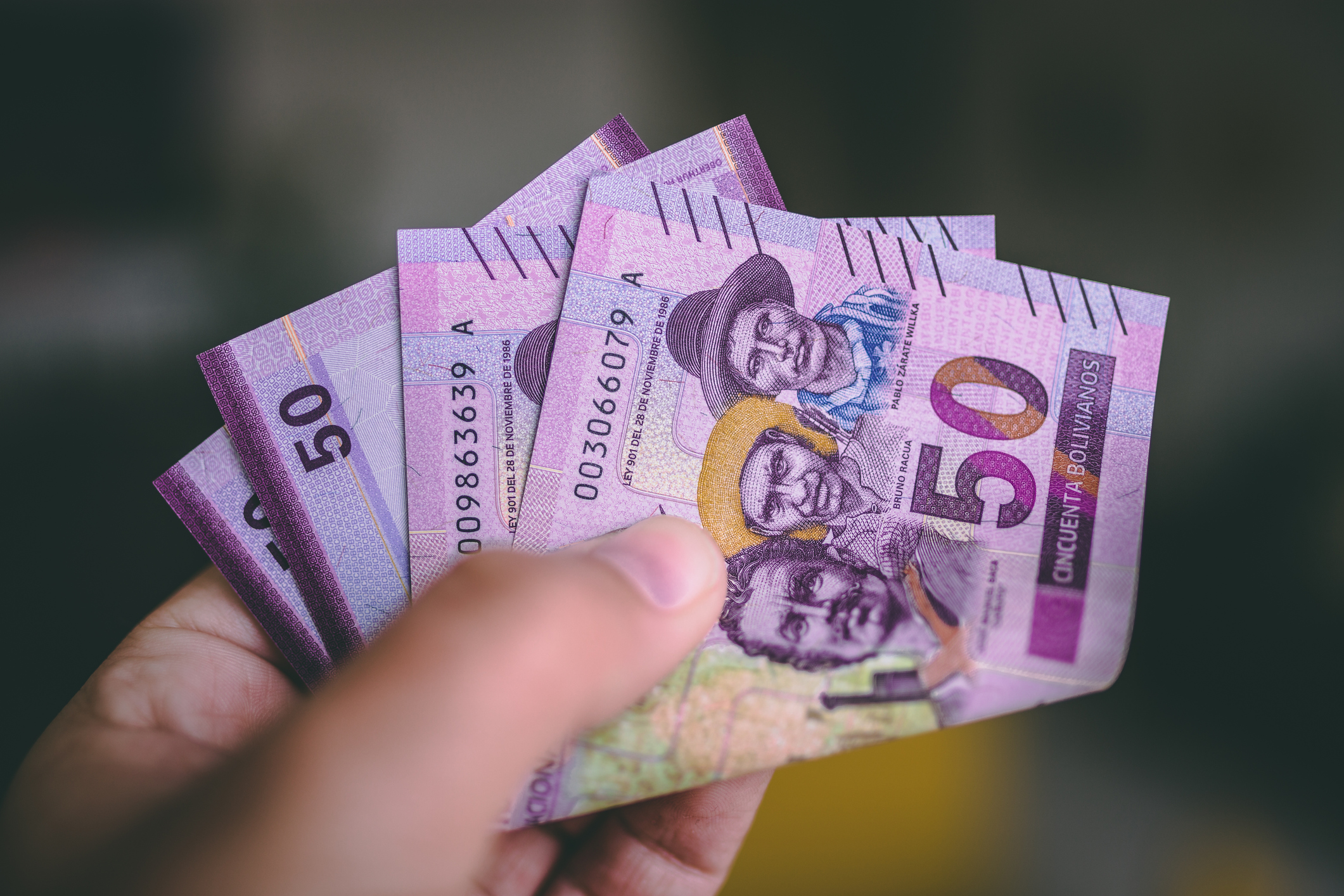 A hand holds several 50-unit banknotes featuring portraits of people, with purple and green designs.