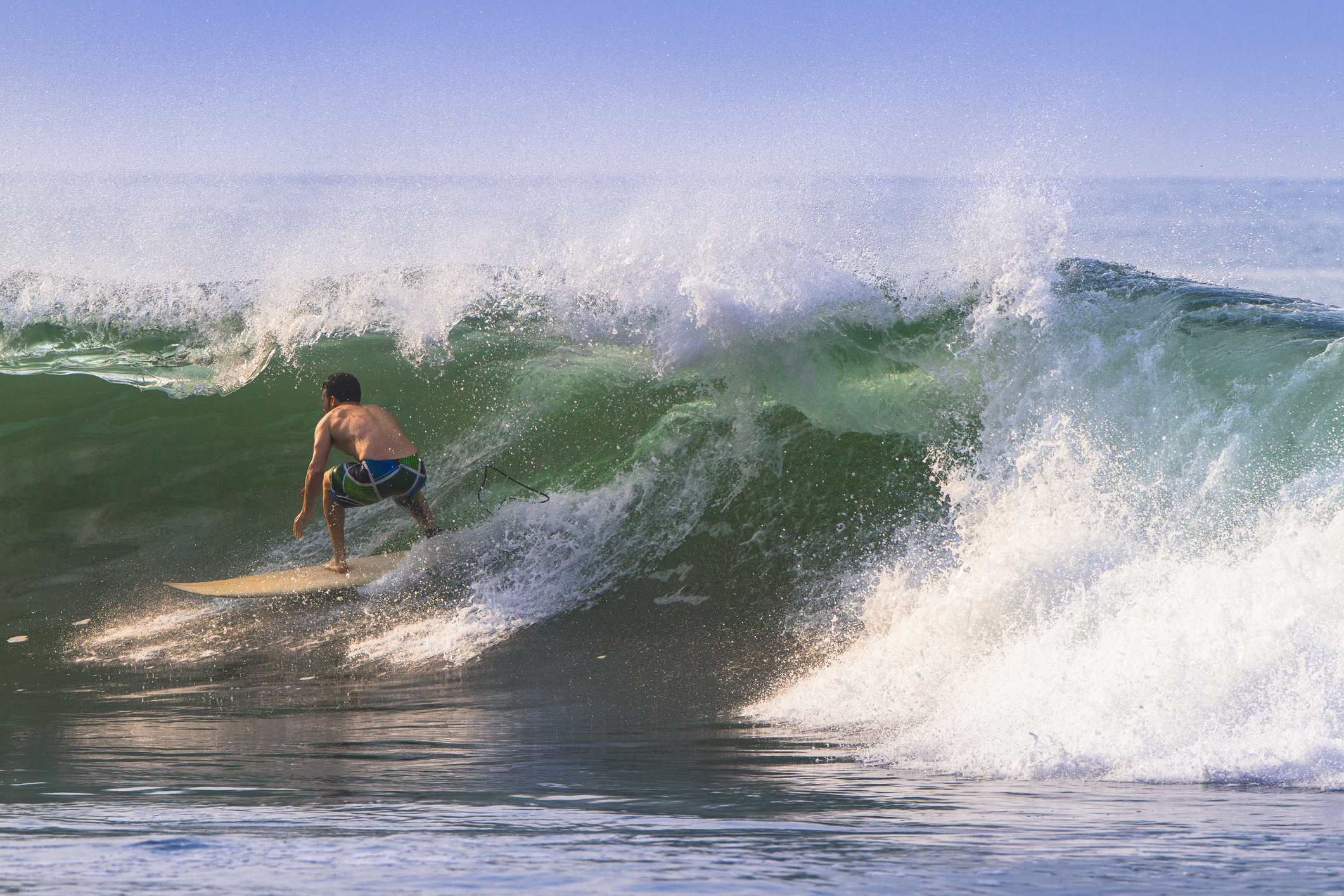 A surfer rides a large wave, skillfully maneuvering on his board as the water crashes around him.