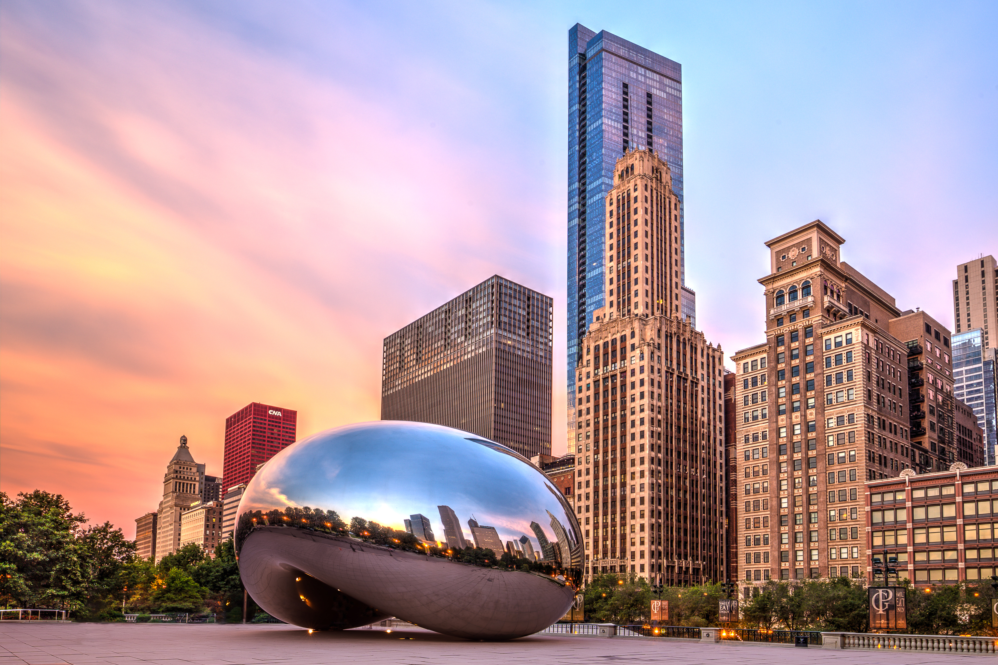 Cloud Gate sculpture reflects the skyline at sunset, surrounded by urban buildings in a vibrant city landscape.