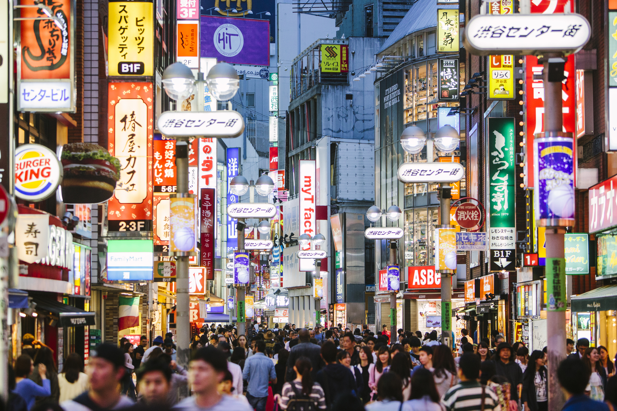 Busy street scene in a city, illuminated by colorful signs and bustling with people.