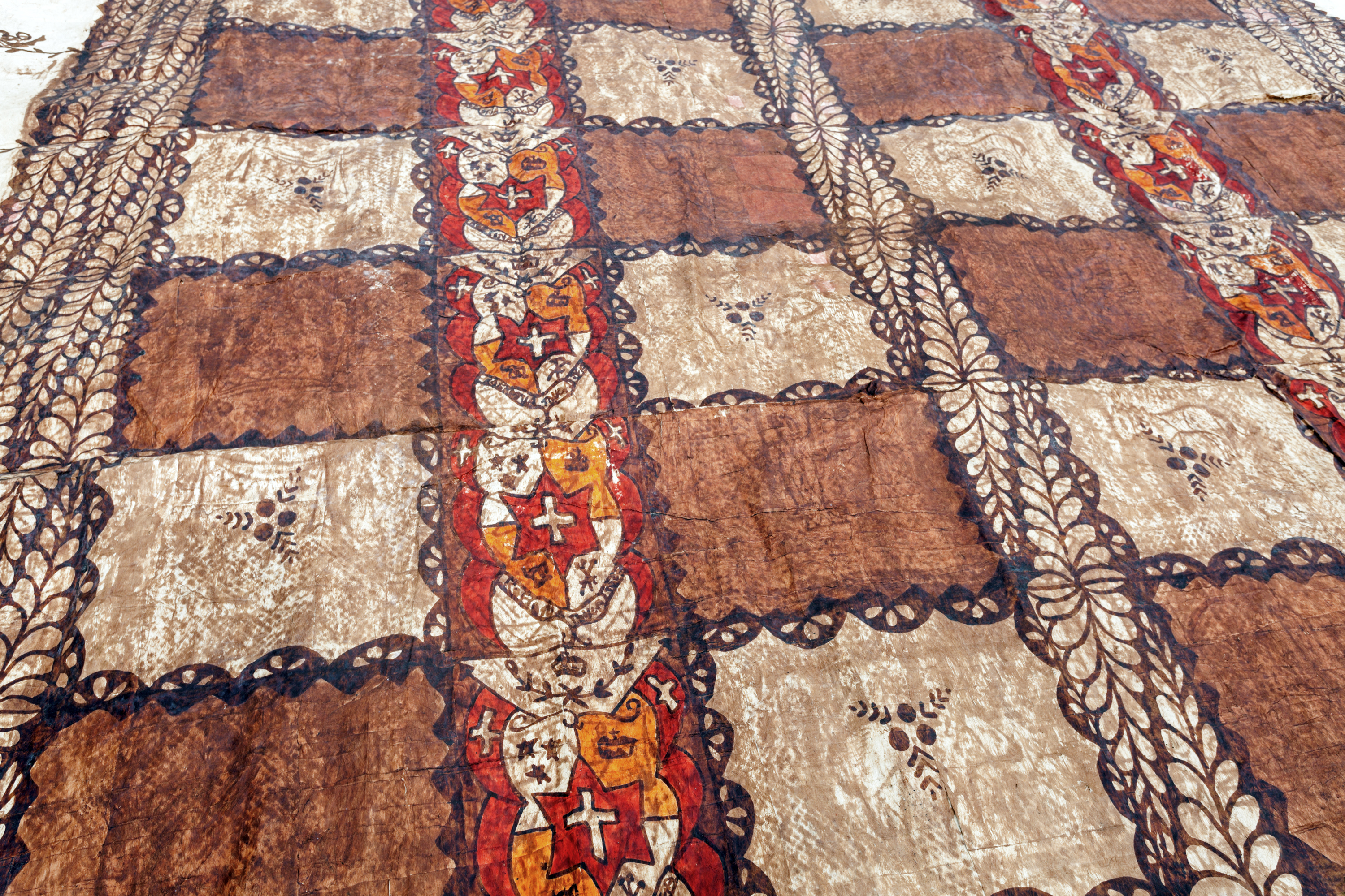 Patterned fabric with alternating brown and beige squares, featuring stylized floral designs and intricate borders.