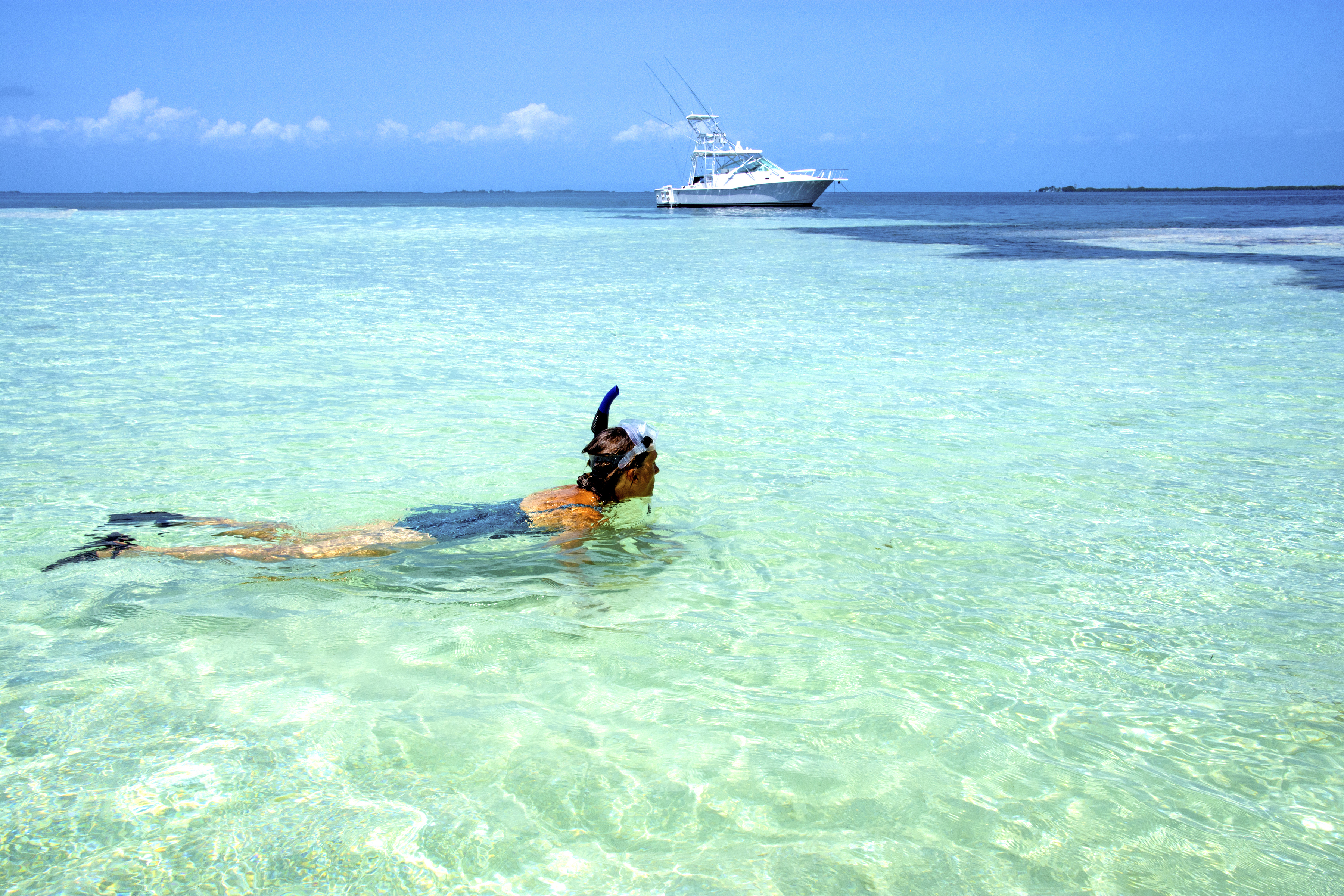 A person snorkels in clear turquoise water, with a boat in the background and a blue sky above.