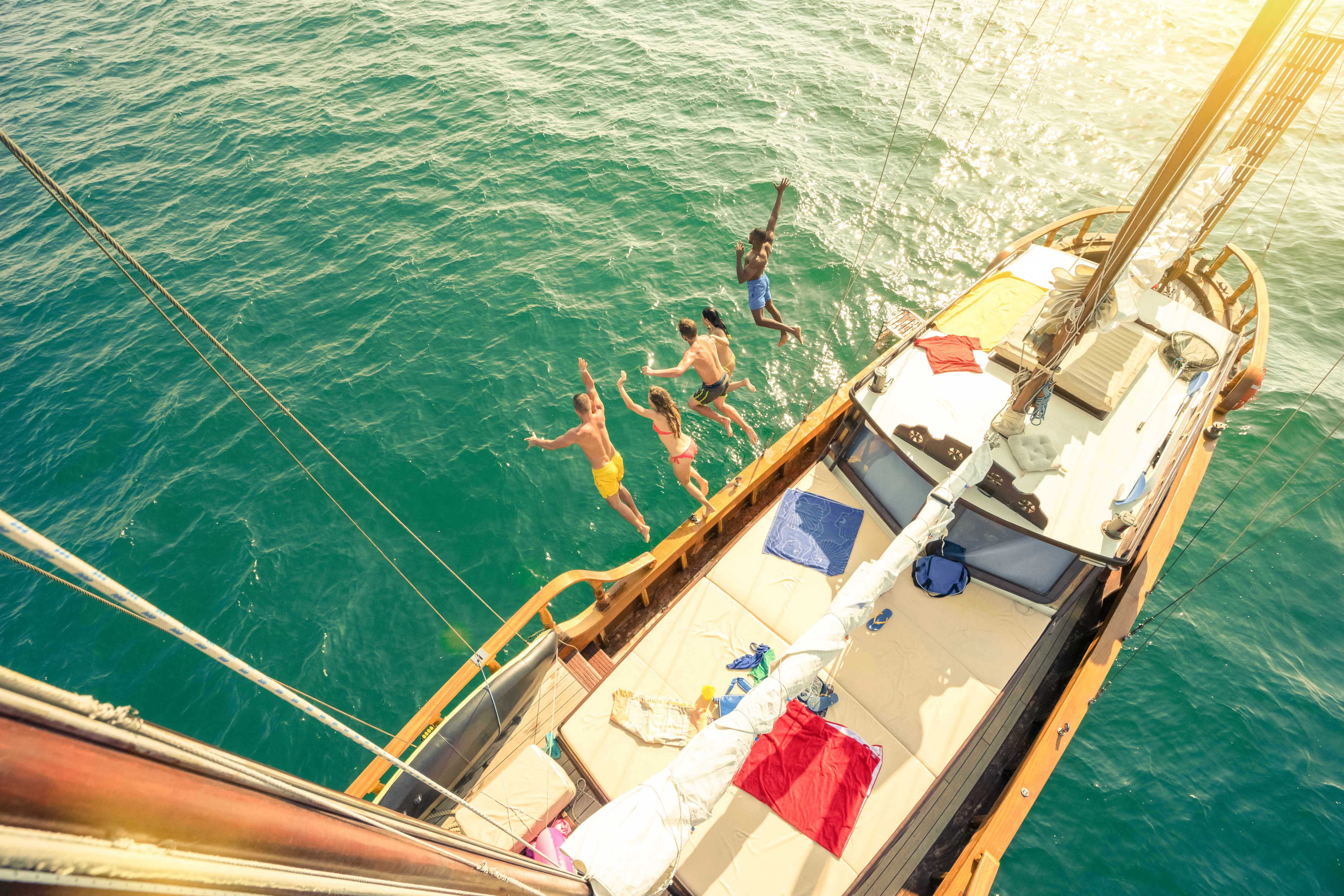 Aerial view of group of people jumping from sailing boat on a day sea trip