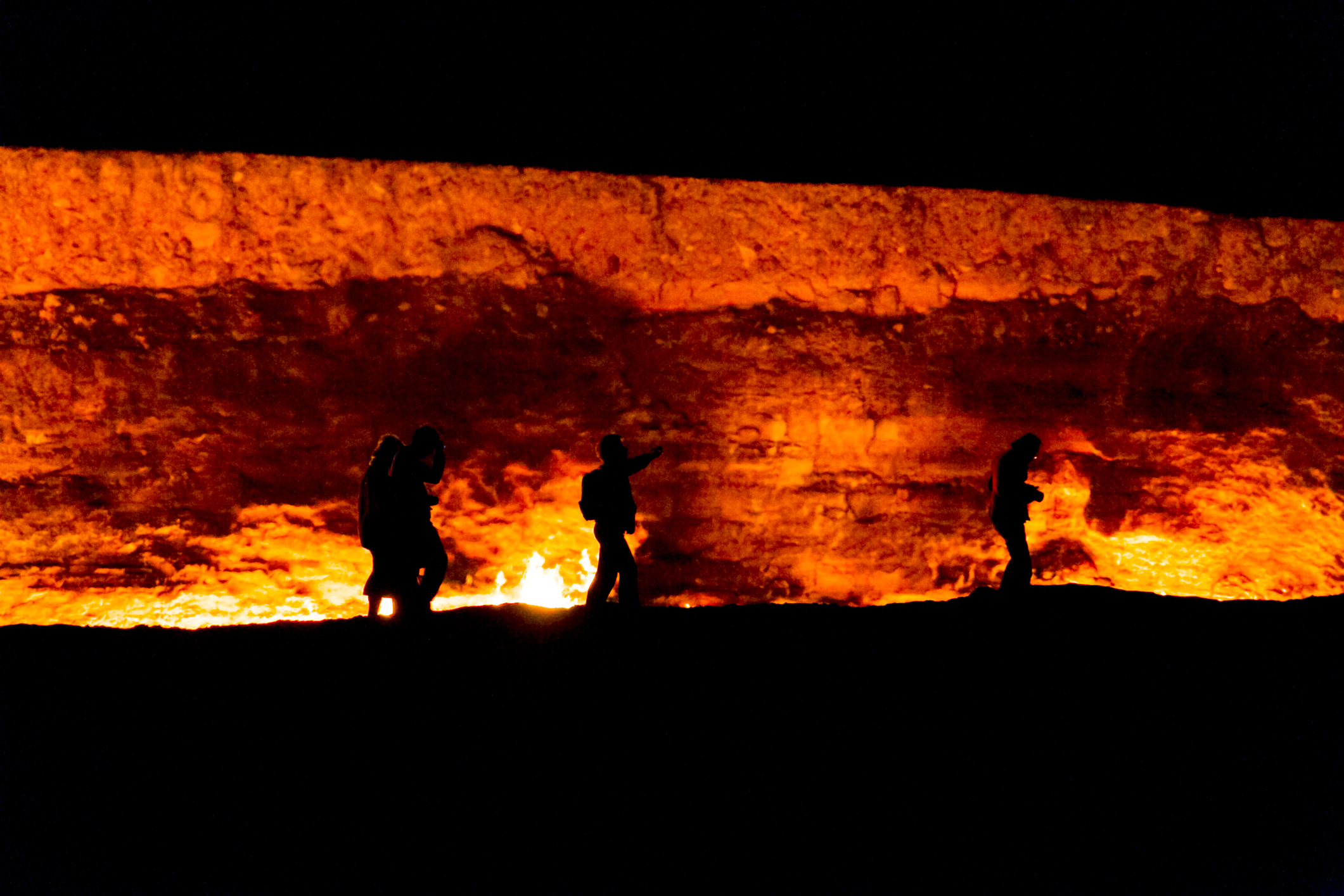 Silhouettes of people walking near a glowing, firelit rock wall at night.