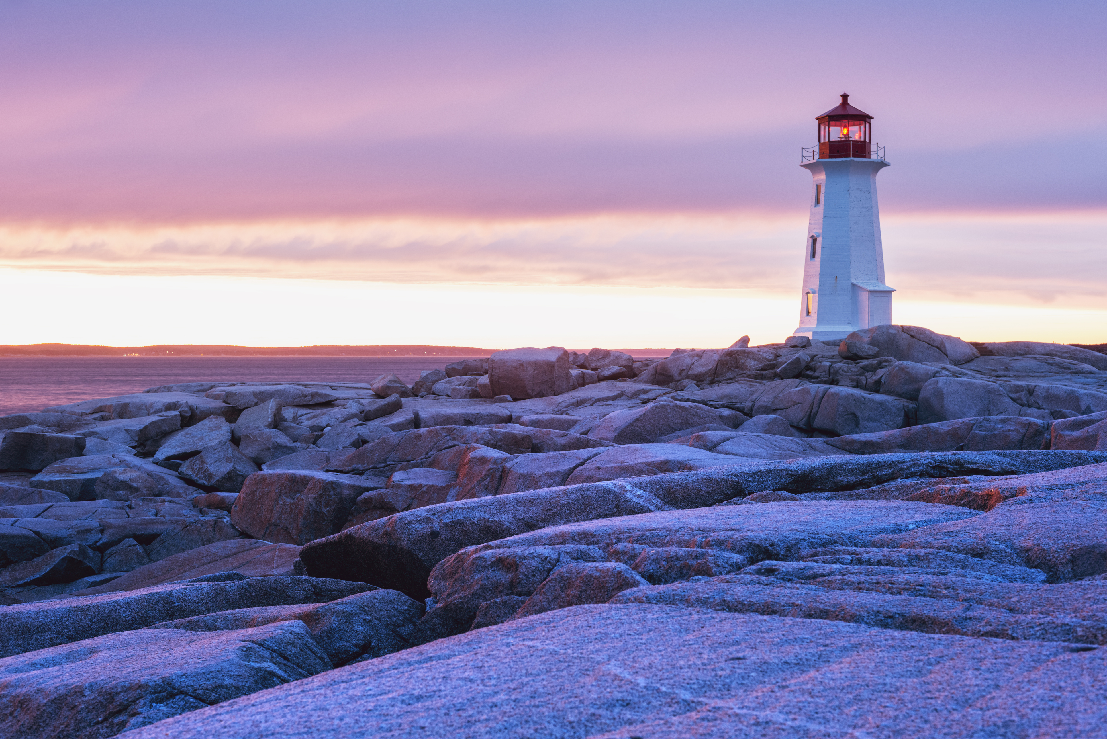 The granite landscape surrounding Peggy's Cove Lighthouse is washed in sunset colours