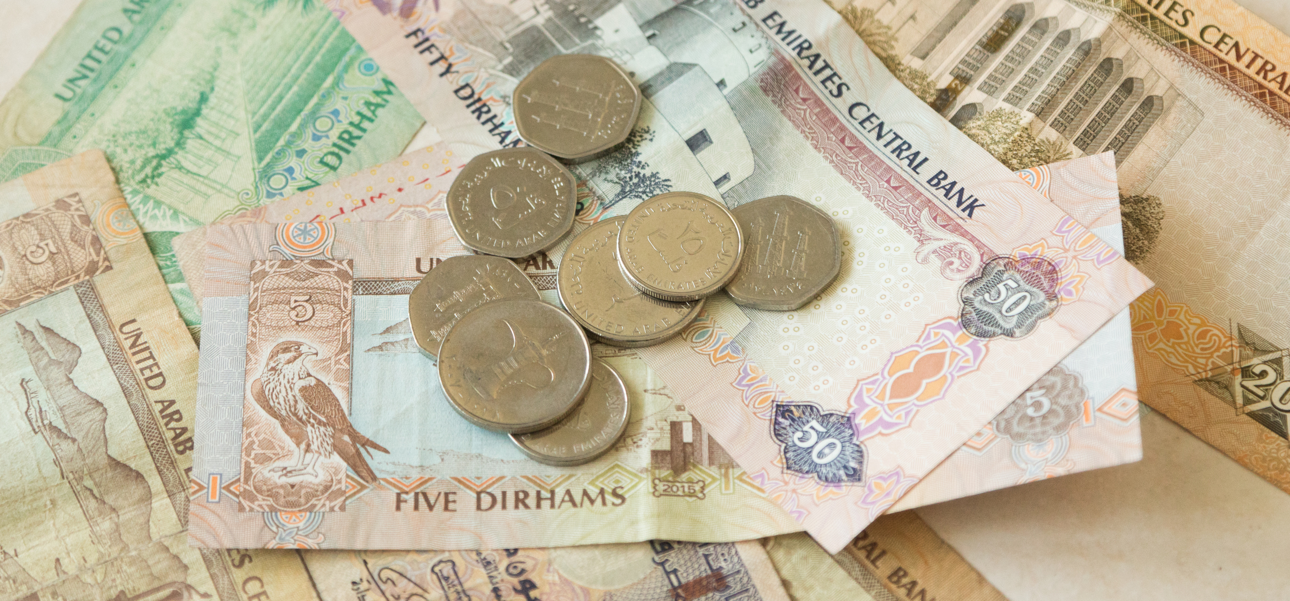 A pile of United Arab Emirates dirham banknotes and coins, featuring various denominations and designs.