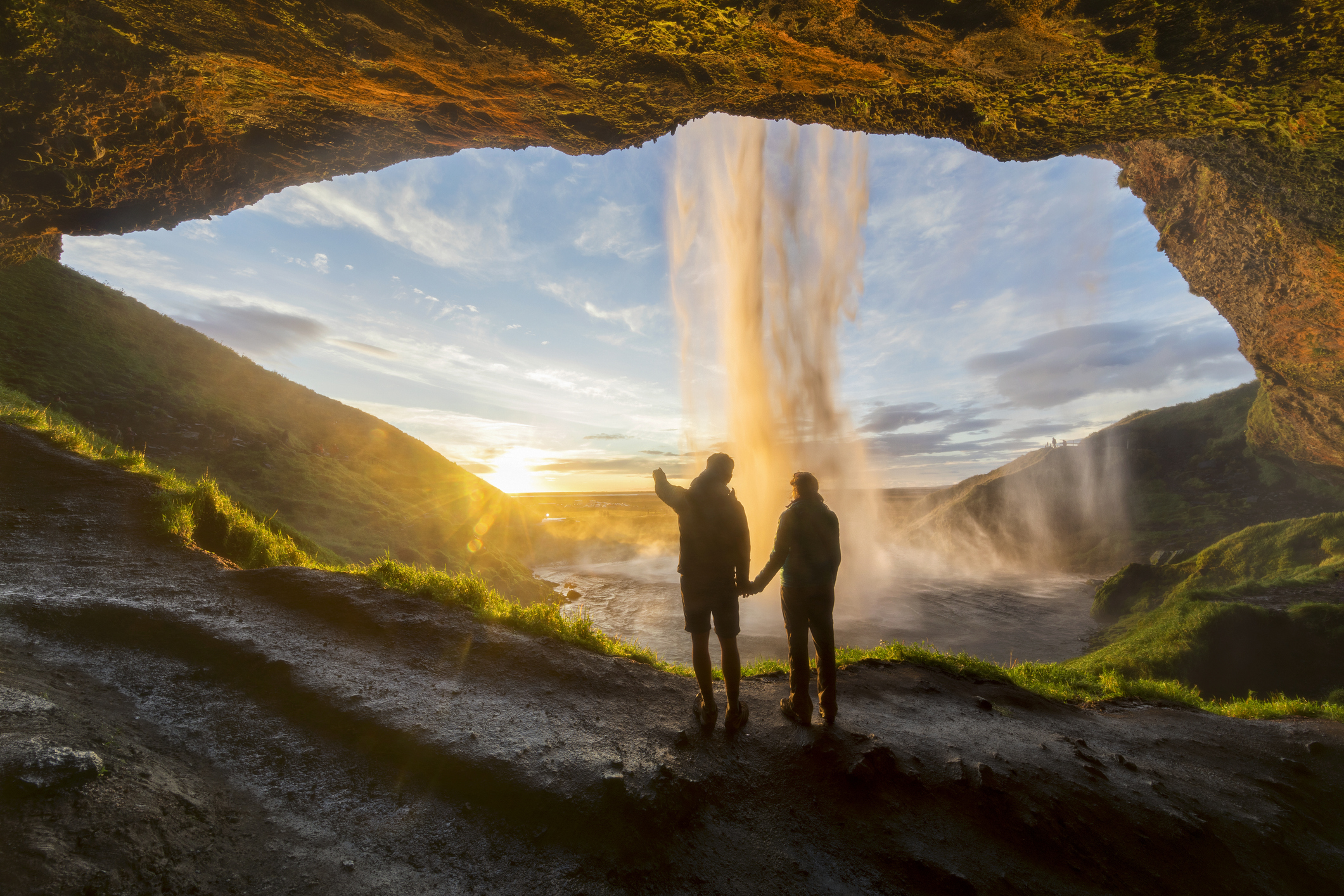 Tourists under waterfall in Seljalandsfoss, Iceland, man pointing with finger to the sun