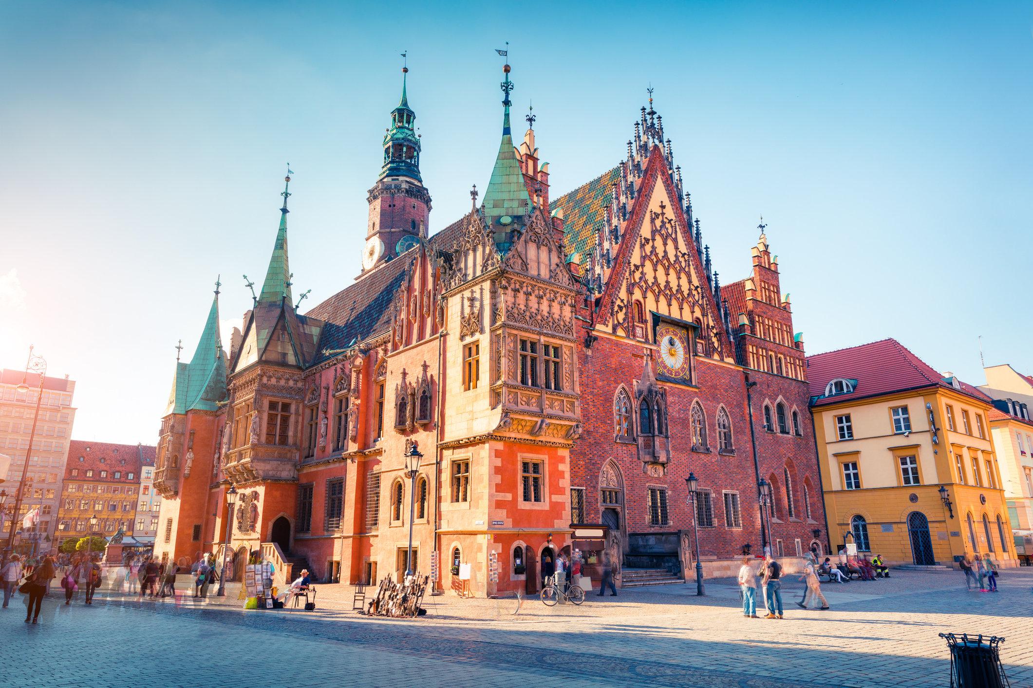Historic building with intricate architectural details, set in a lively square filled with people and shops.