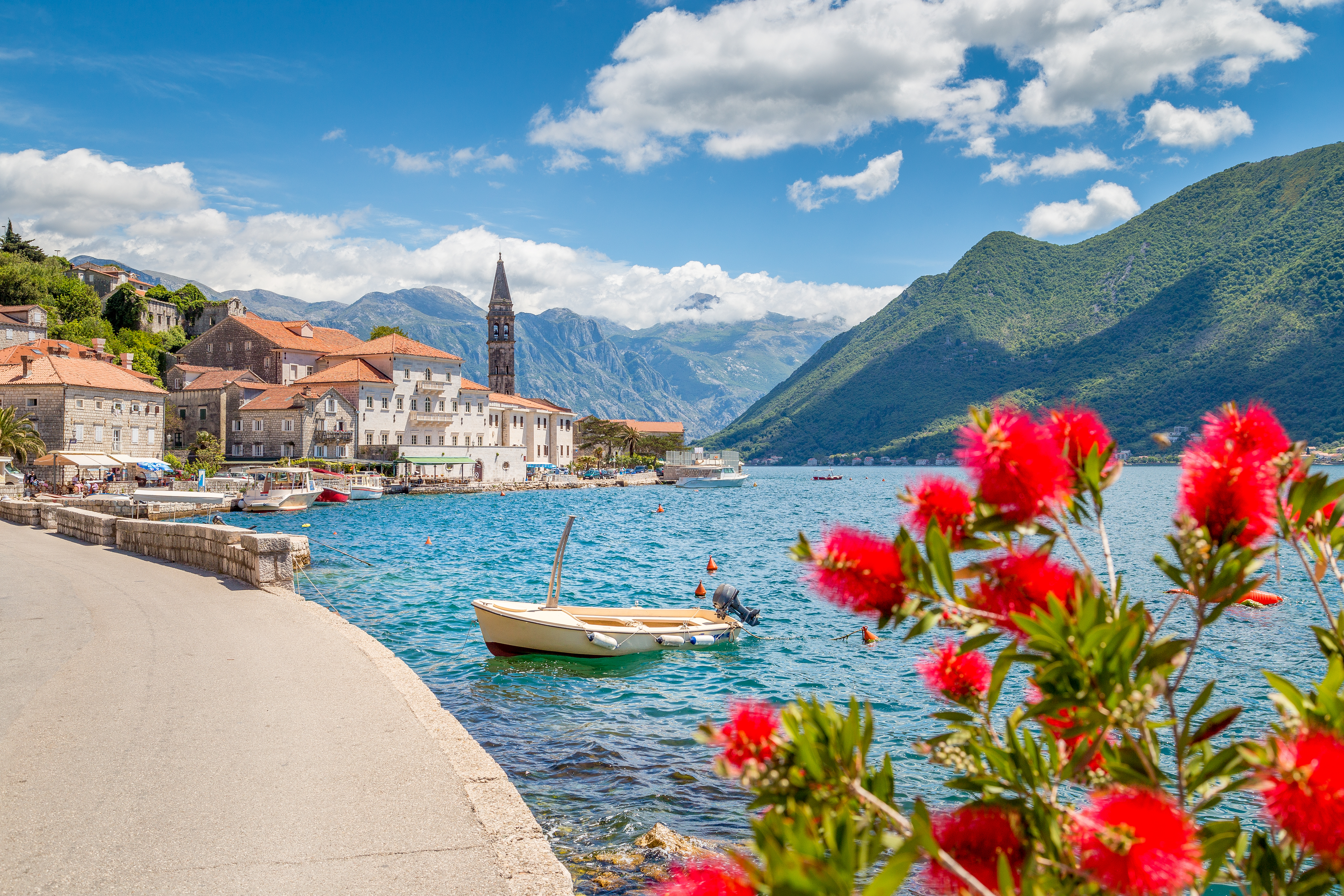 Panorama view of Perast at famous Bay of Kotor with blooming flowers on a beautiful sunny day with blue sky and clouds in summer