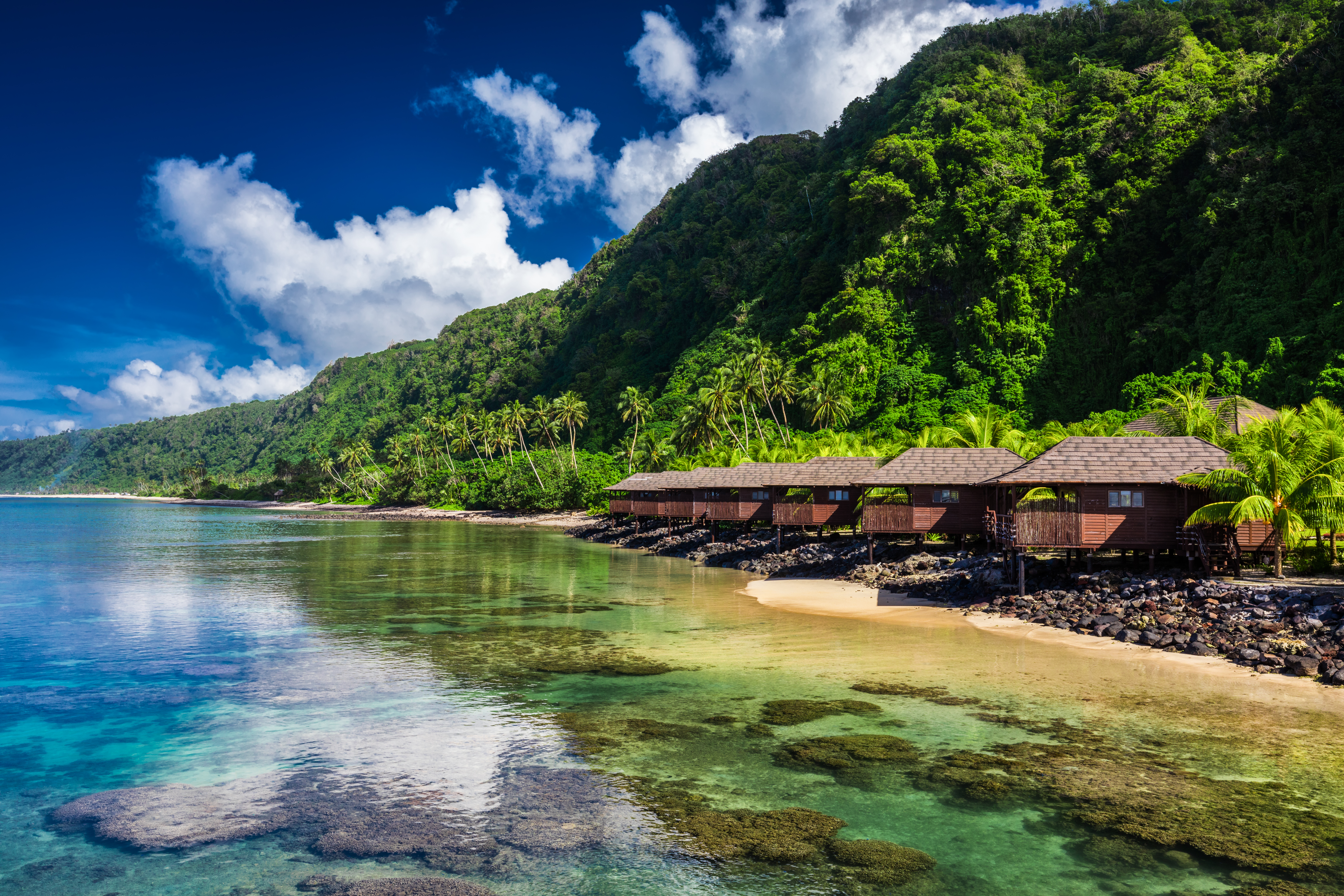 Small beach houses line the shore with green vegetation behind them