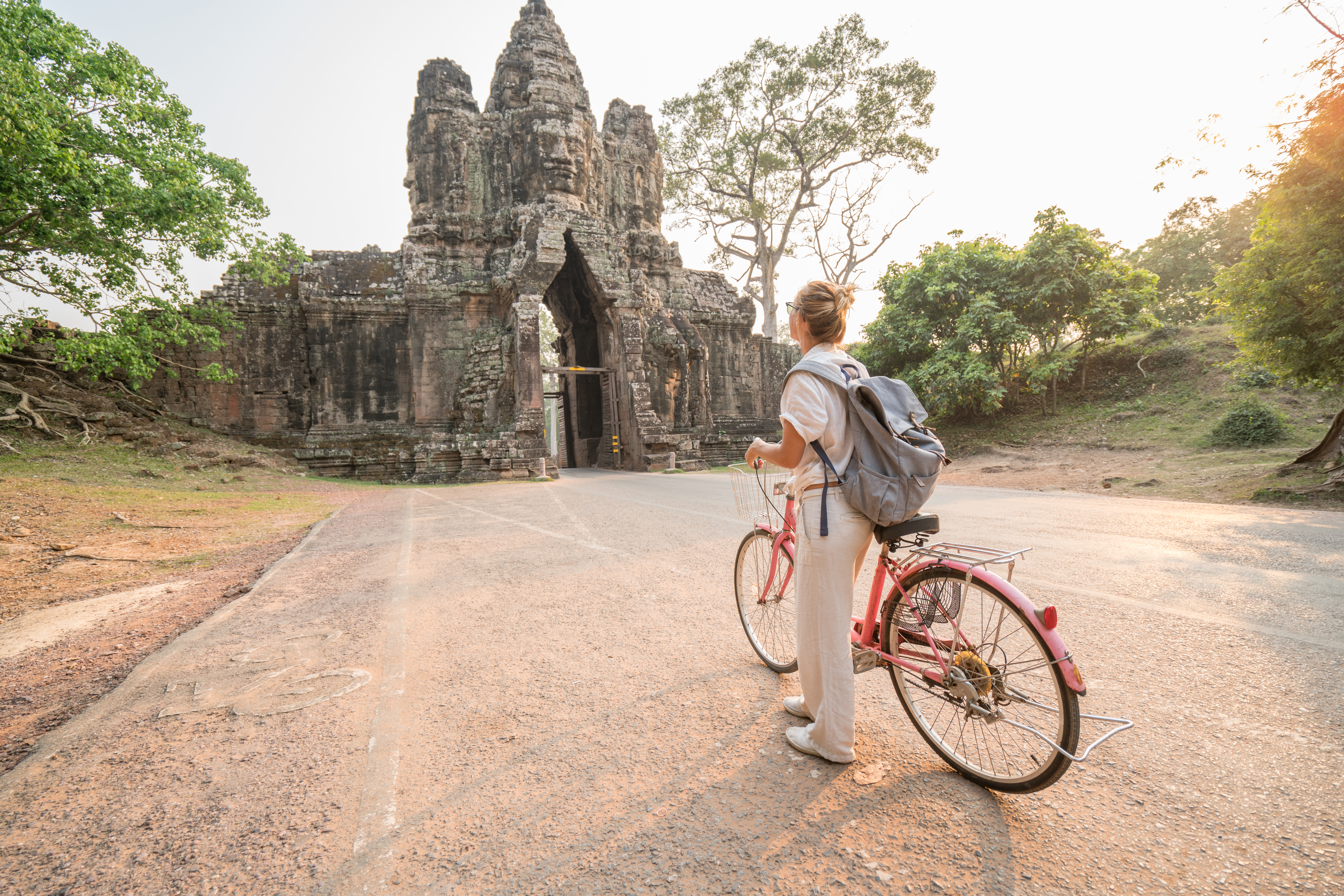 Young woman traveling in Cambodia visiting the temples of Angkor wat complex by bicycle.