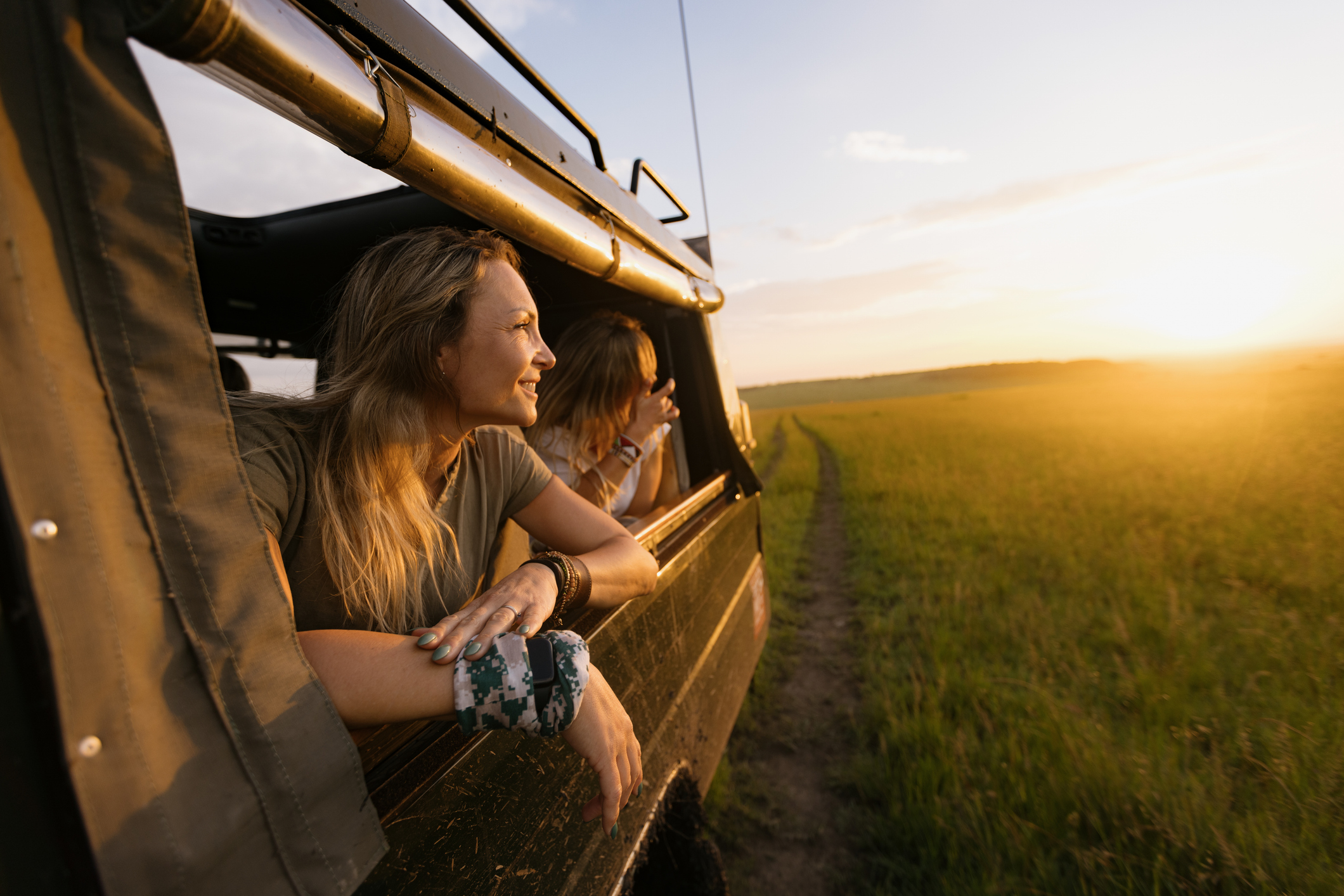 A woman in a Land Cruiser on a safari game drive at sunset leaning out of the vehicle window.