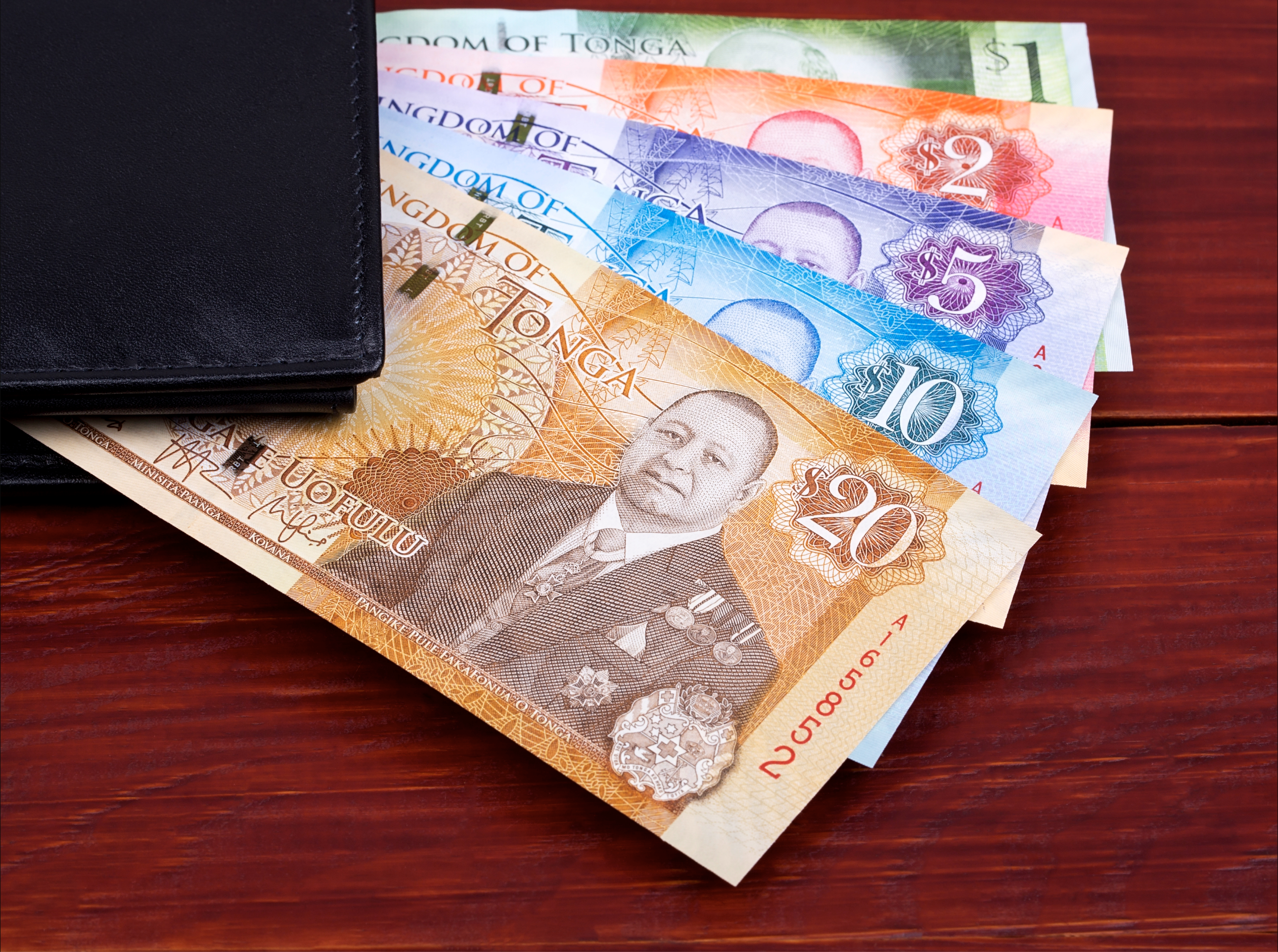 A wallet with Tongan banknotes in various denominations displayed on a wooden surface.