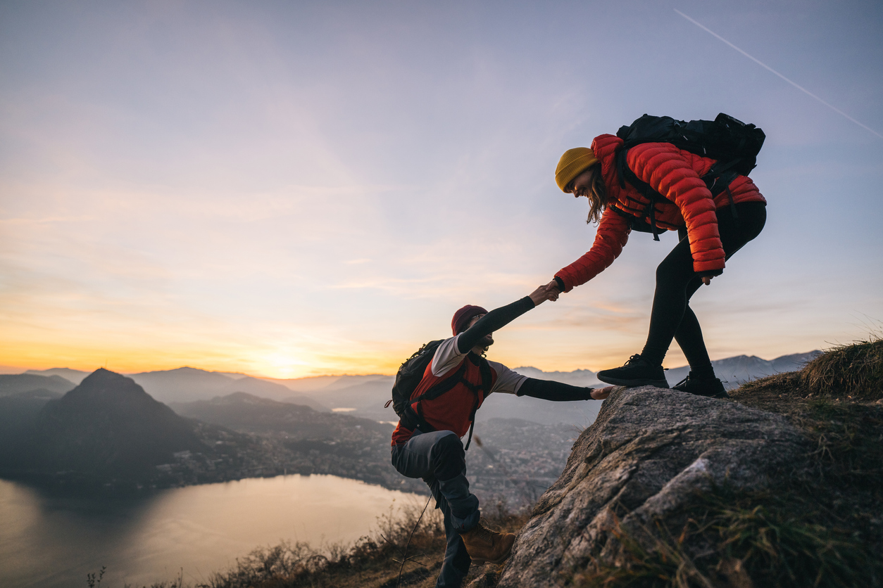 People helping one another climb a mountain