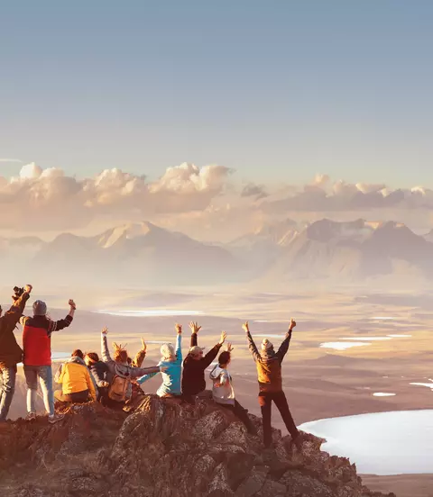 Group celebrating hiking to reach top of mountain top looking out at mountain's valley