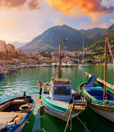 Fishing boats docked in the lovely seaside village with mountains and sun in the background