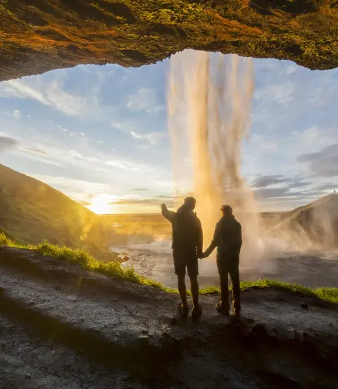 Tourists under waterfall in Seljalandsfoss, Iceland, man pointing with finger to the sun