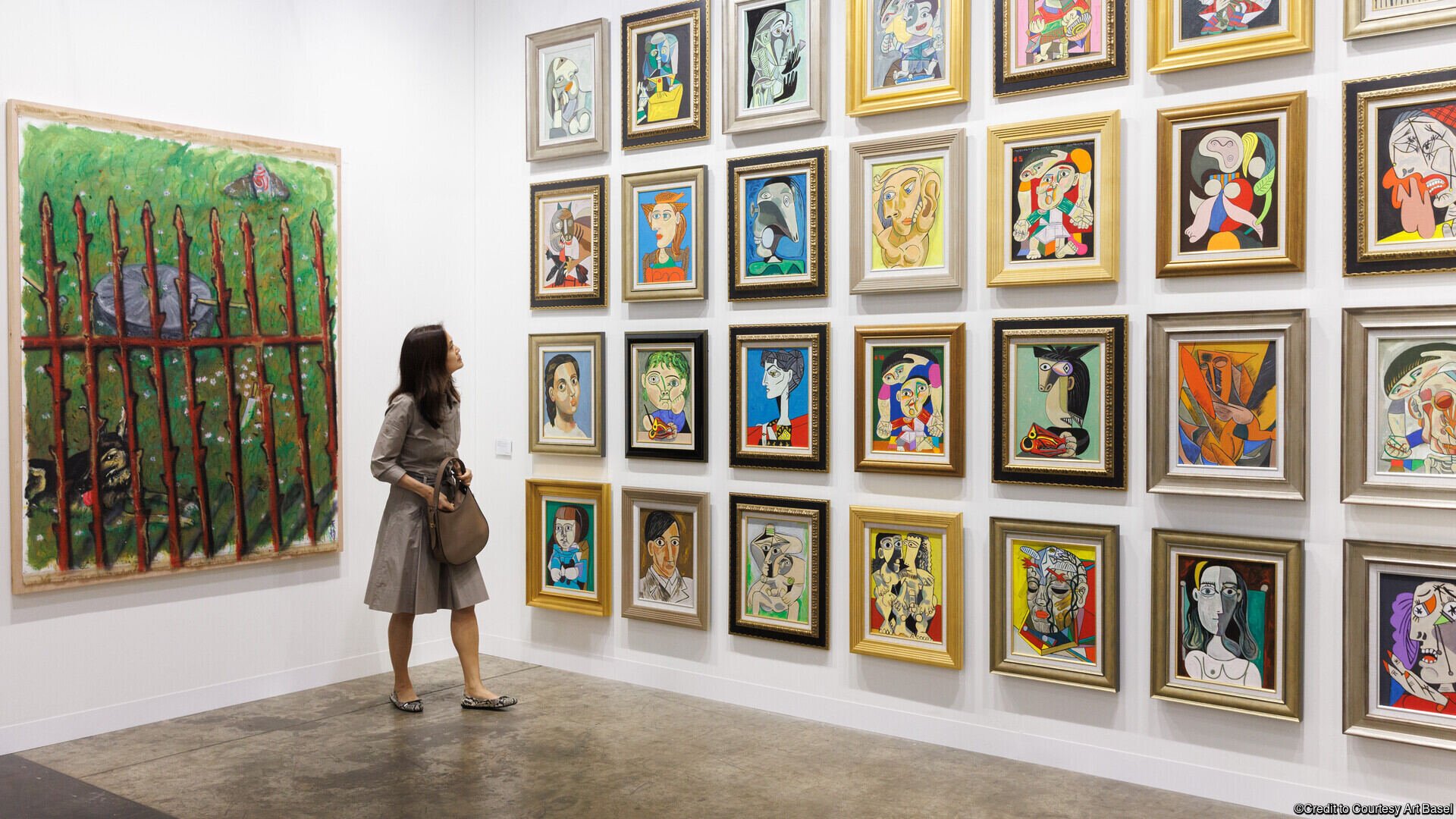 A woman observes a wall of colorful, framed abstract portraits in a modern art gallery.