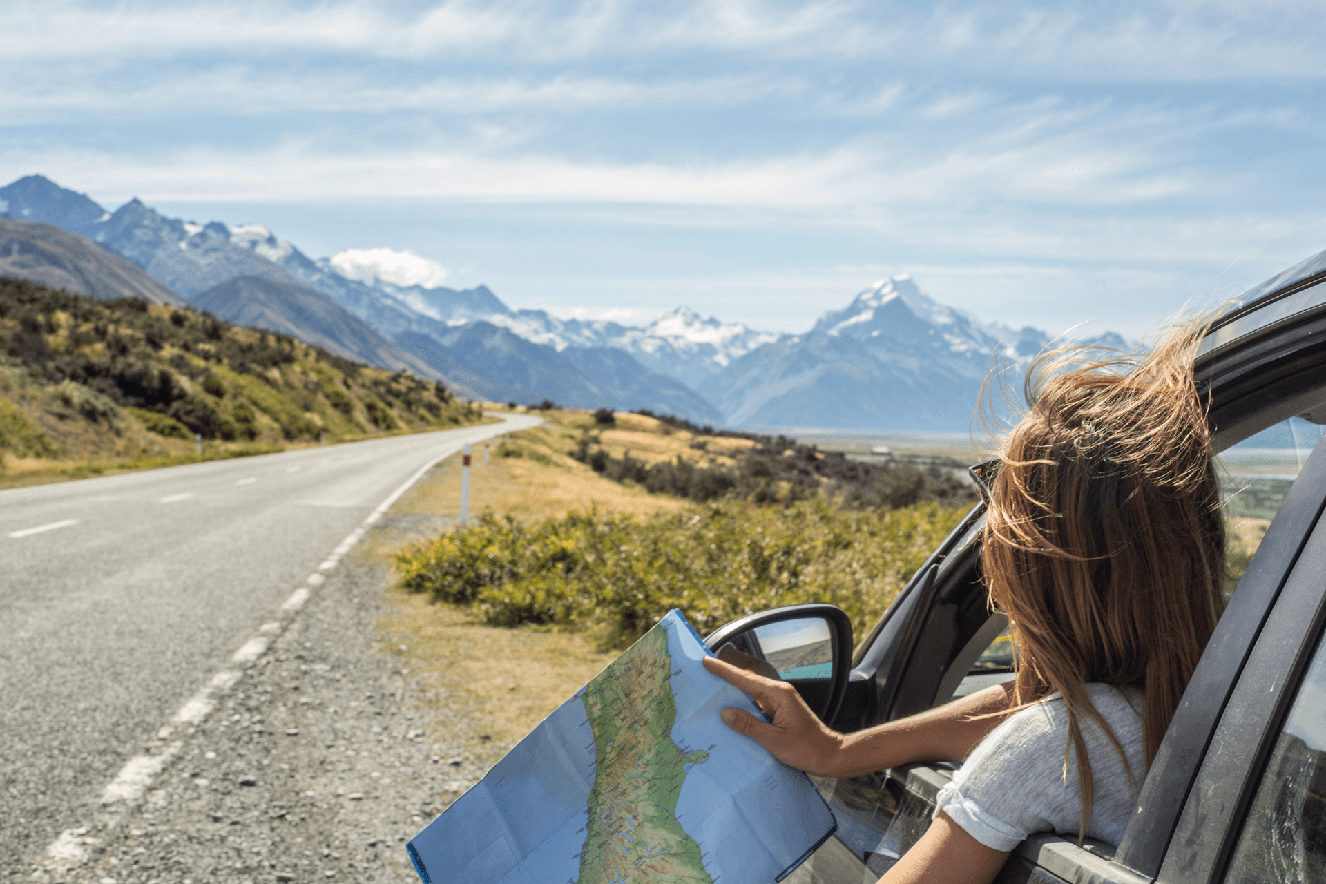 Woman in a car along a highway overlooking a beautiful view, checking a map for directions