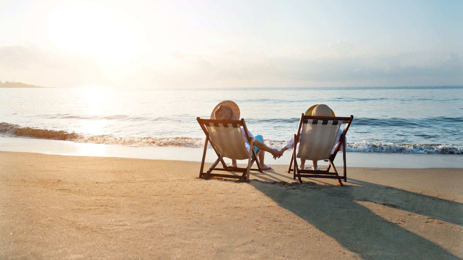 Couple sitting on deck chairs at beach during sunset, watching waves roll in