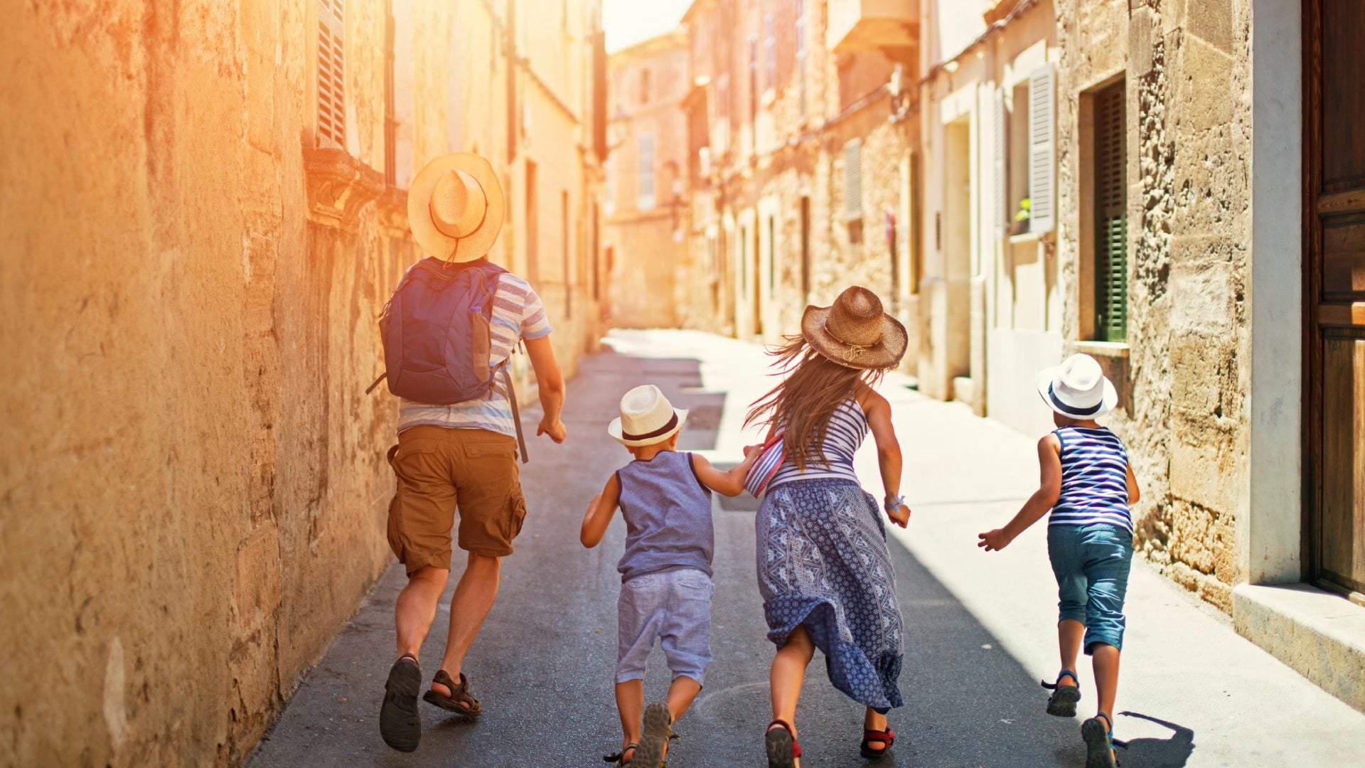 Father and kids running beautiful street of a mediterranean town. Sunny summer day. Pollenca, Mallorca, Spain.