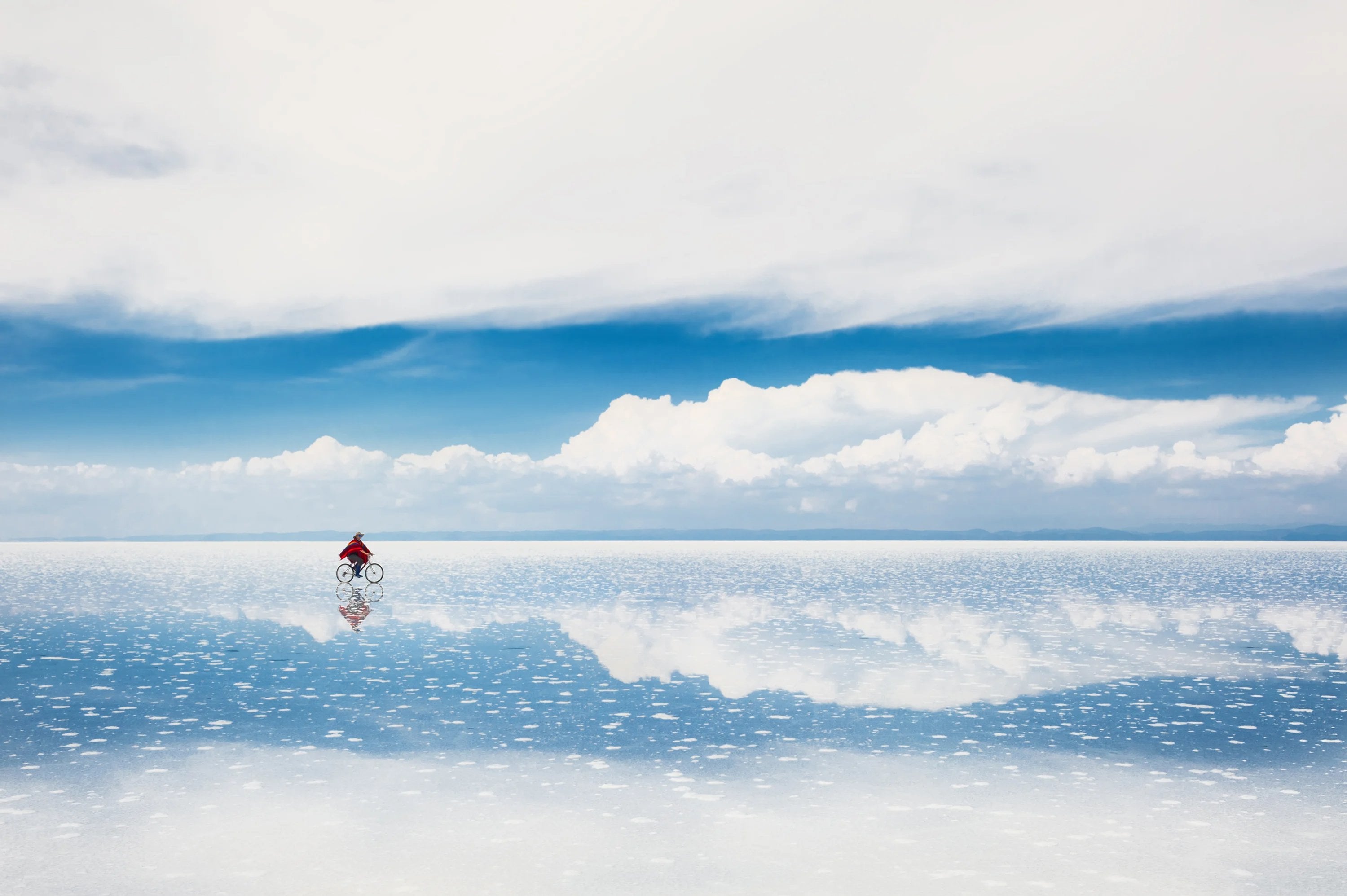 Person walking across salt flats reflecting the sky