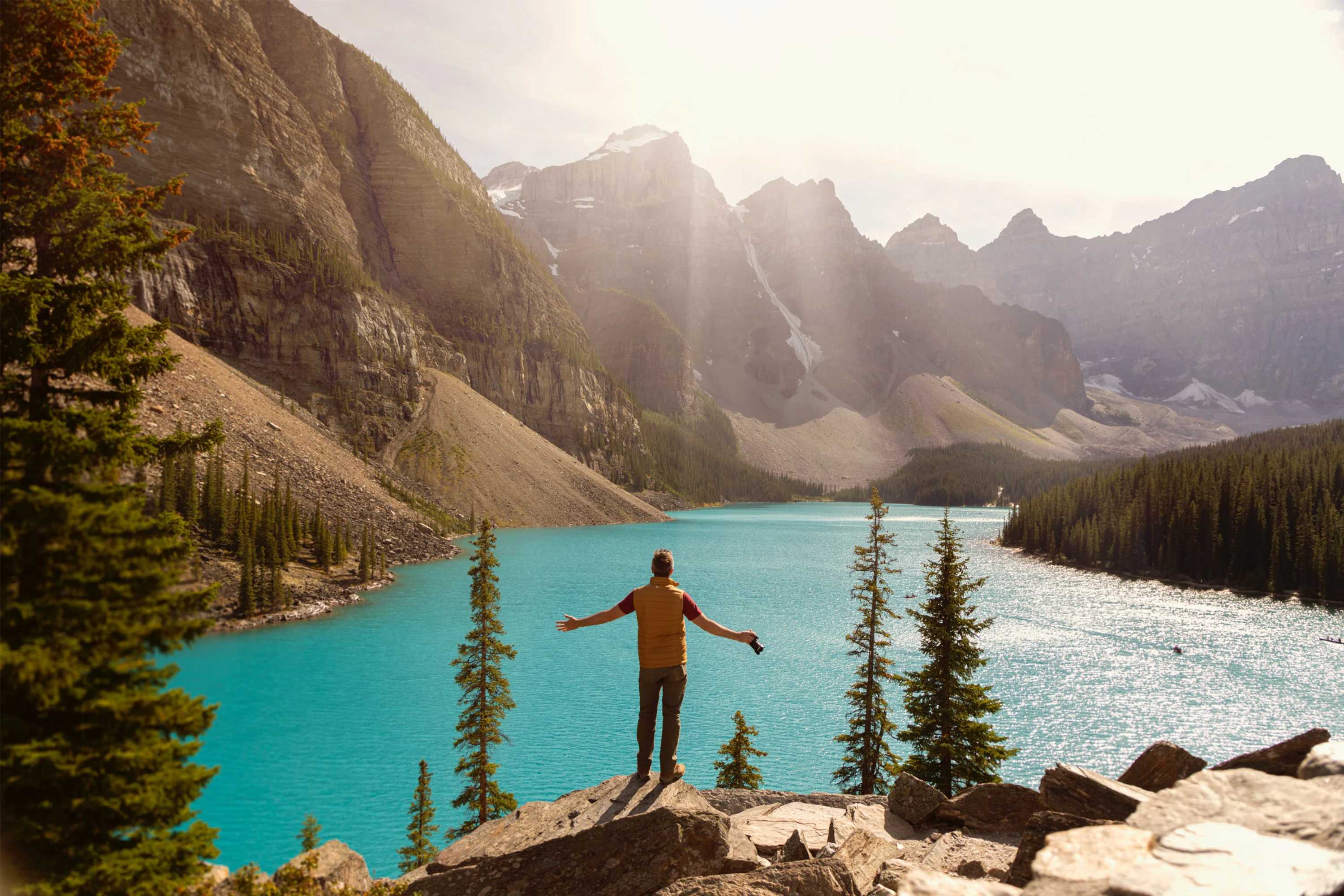 Person standing on the edge of rocks overlooking a clear blue lake with mountain backdrops.