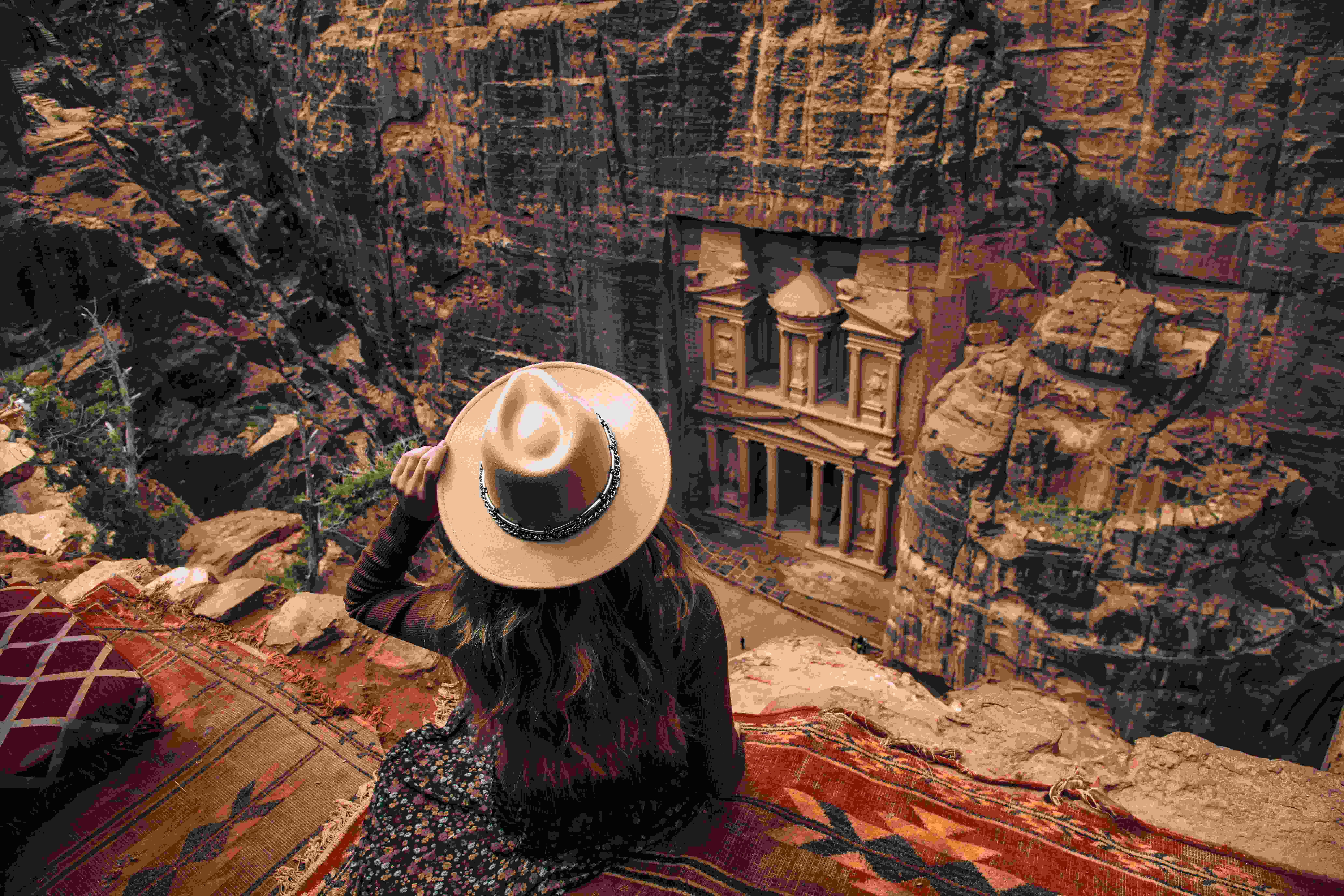 Woman with a hat sitting on the edge of a cliff overlooking a carved tomb