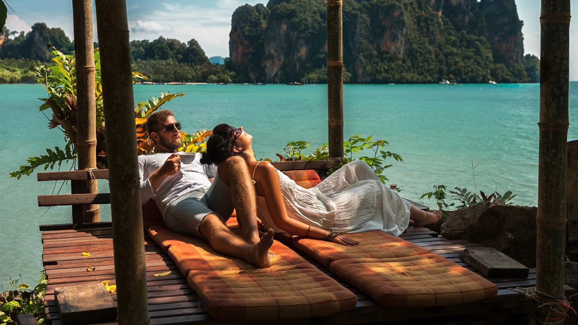 Couple relaxing together in a sea-side bungalow, surrounded by lush greenery.