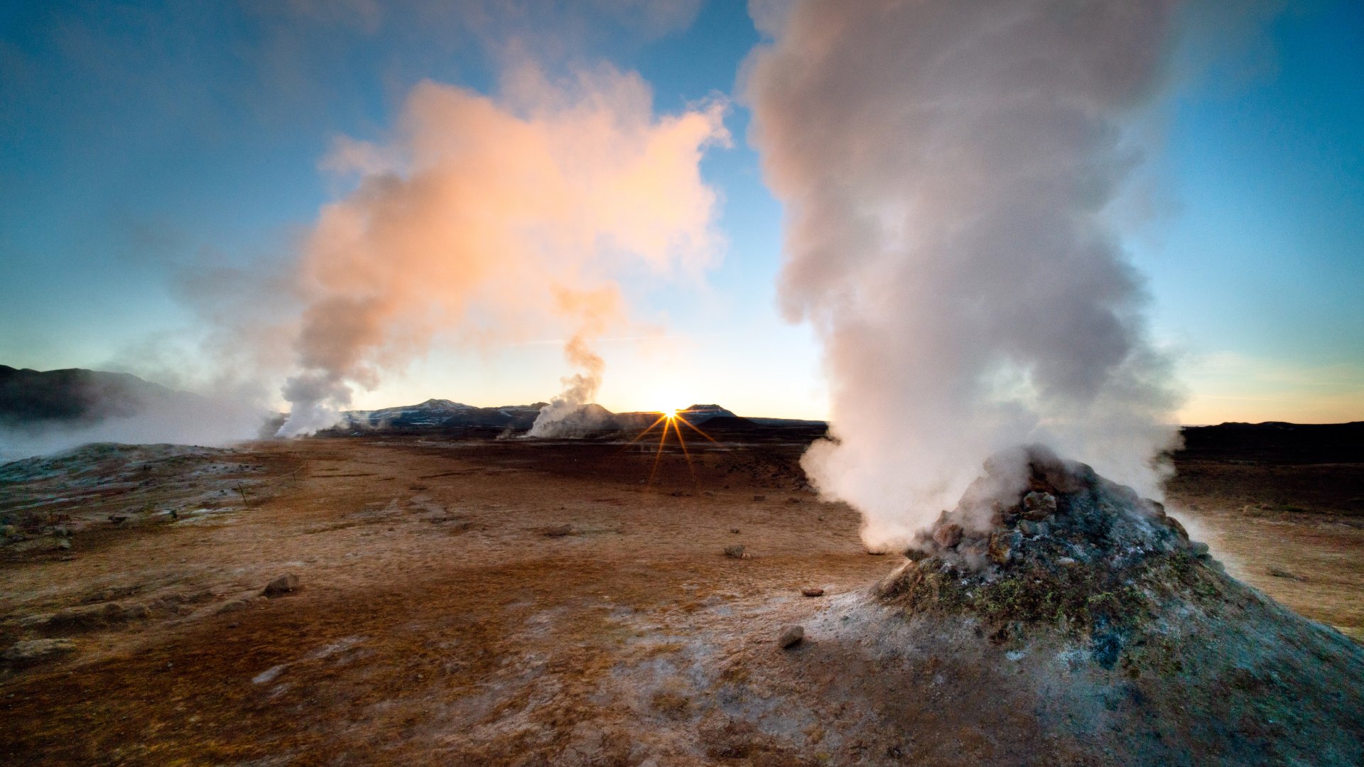 Iceland A beautiful dawn in Iceland, a country with many geothermal features including these dramatic fumaroles. Shot with a wide angle lens for dramatic effect and a small aperture to create a sunstar where the sun is just peaking over the horizon. The scenery in Iceland is spectacular and it is becoming a popular tourist destination.