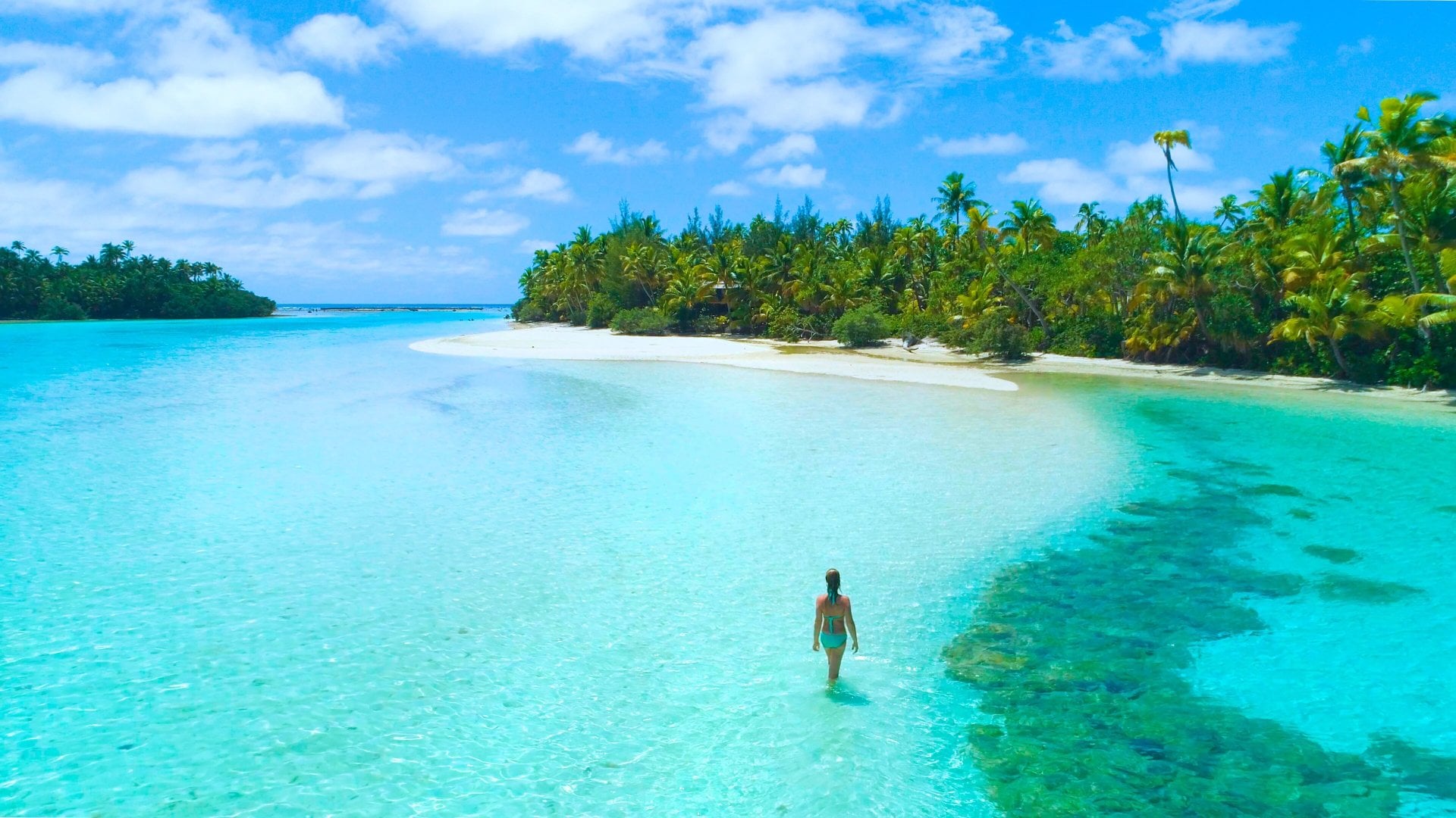 A woman walks through the surf in the clear lagoon of One Foot Island off Aitutaki in the Cook Islands.