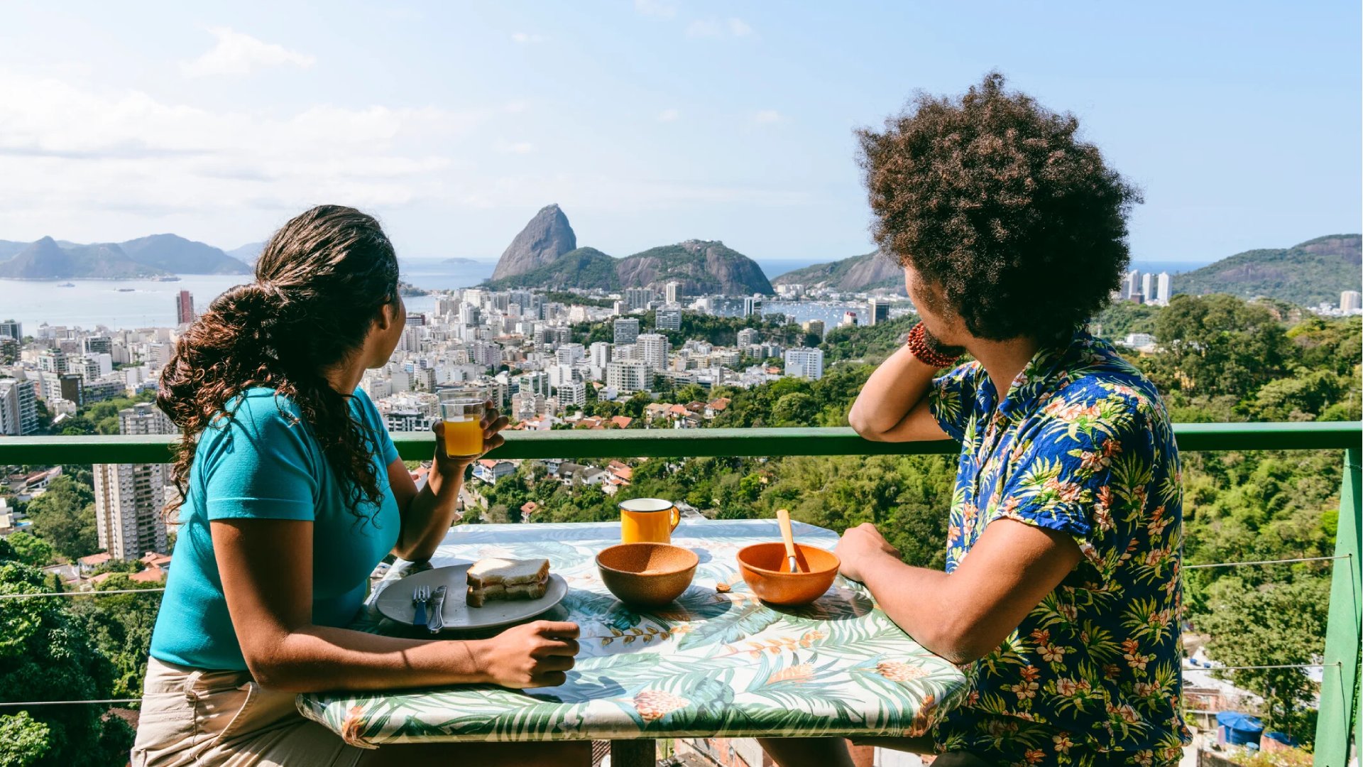 A couple on holiday enjoying a meal in Rio de Janeiro, Brazil, overlooking Sugarloaf mountain from an outdoor rooftop cafe.
