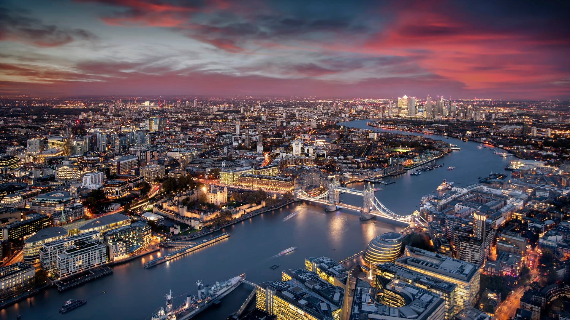 Aerial view of illuminated London, UK, during evening time featuring the Tower Bridge, Thames river and the modern skyscrapers of Canary Wharf
