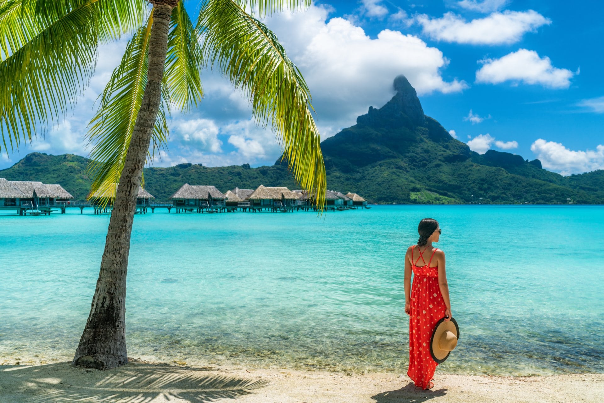 Bora Bora luxury hotel vacation tourist woman relaxing by ocean beach with view of Mt Otemanu in Tahiti, French Polynesia. High End resort with overwater bungalows villas.