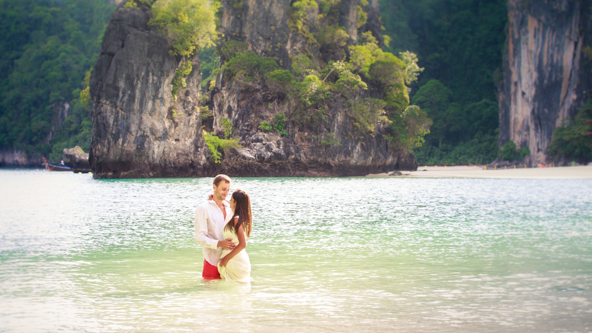 Couple stand in sea water in island bay with karst in background, Thailand