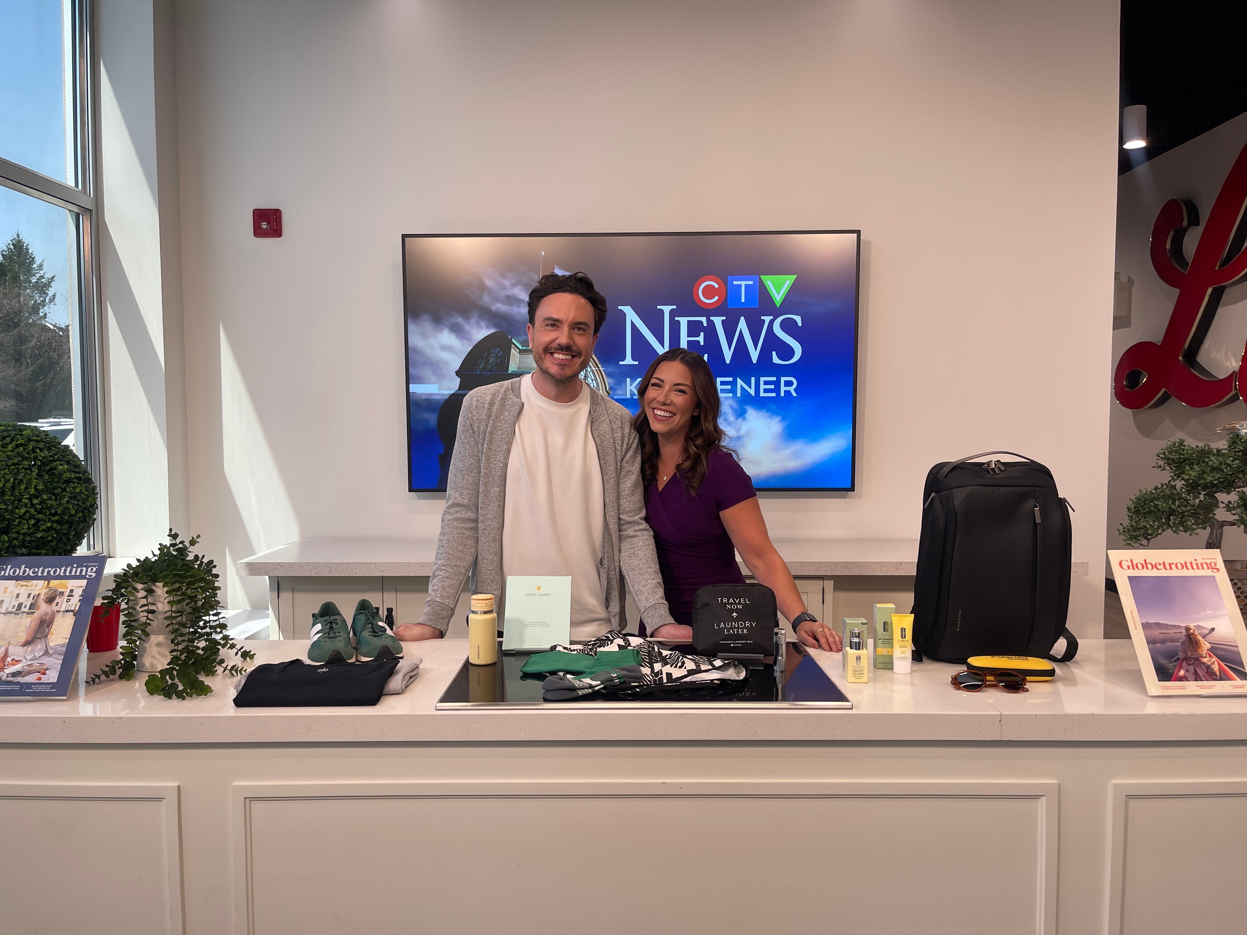 Mitchell Fawcette, Editor-in-Chief of Globetrotting Magazine, and Leighanne Evans of CTV KW Evening News in Kitchener smiling before their local news segment.