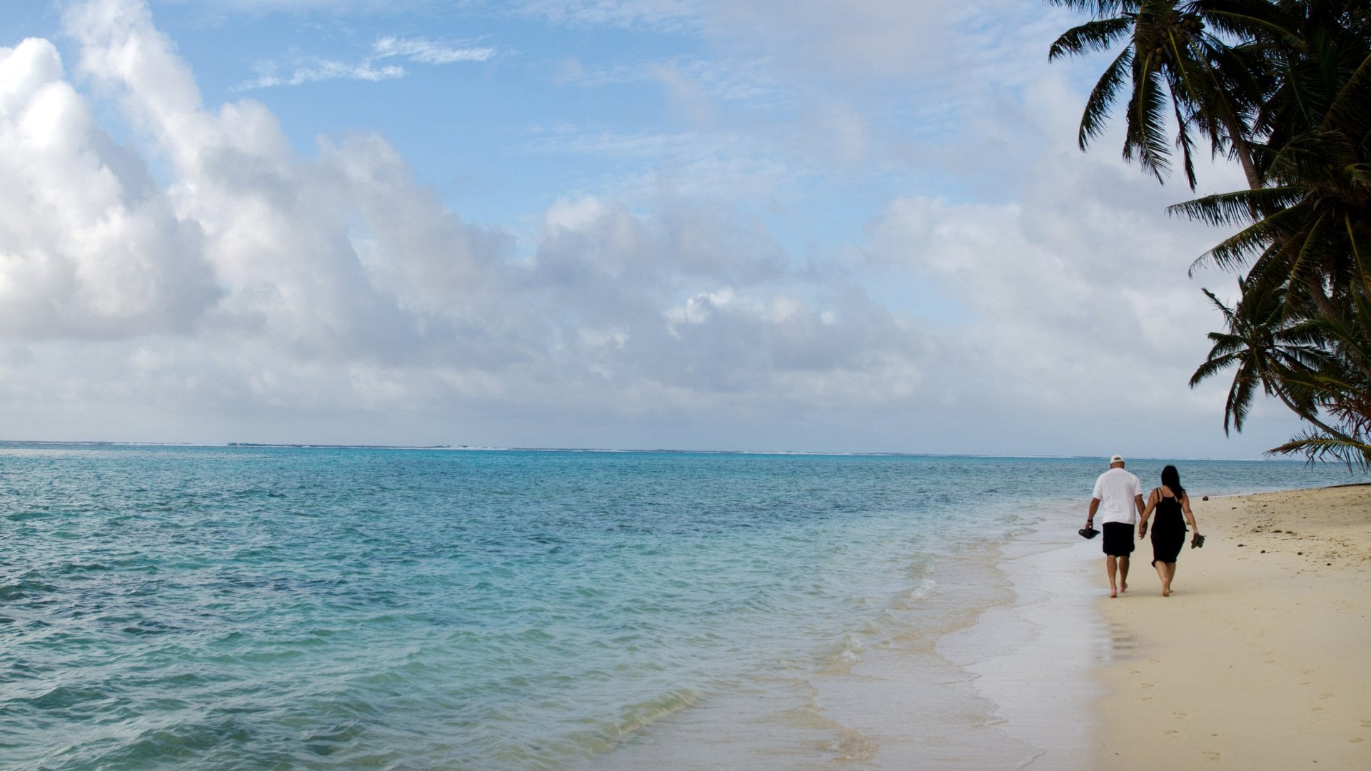 Pacific Islander couple walks on the beach at Muri Lagoon in Rarotonga Cook Islands during sunrise.
