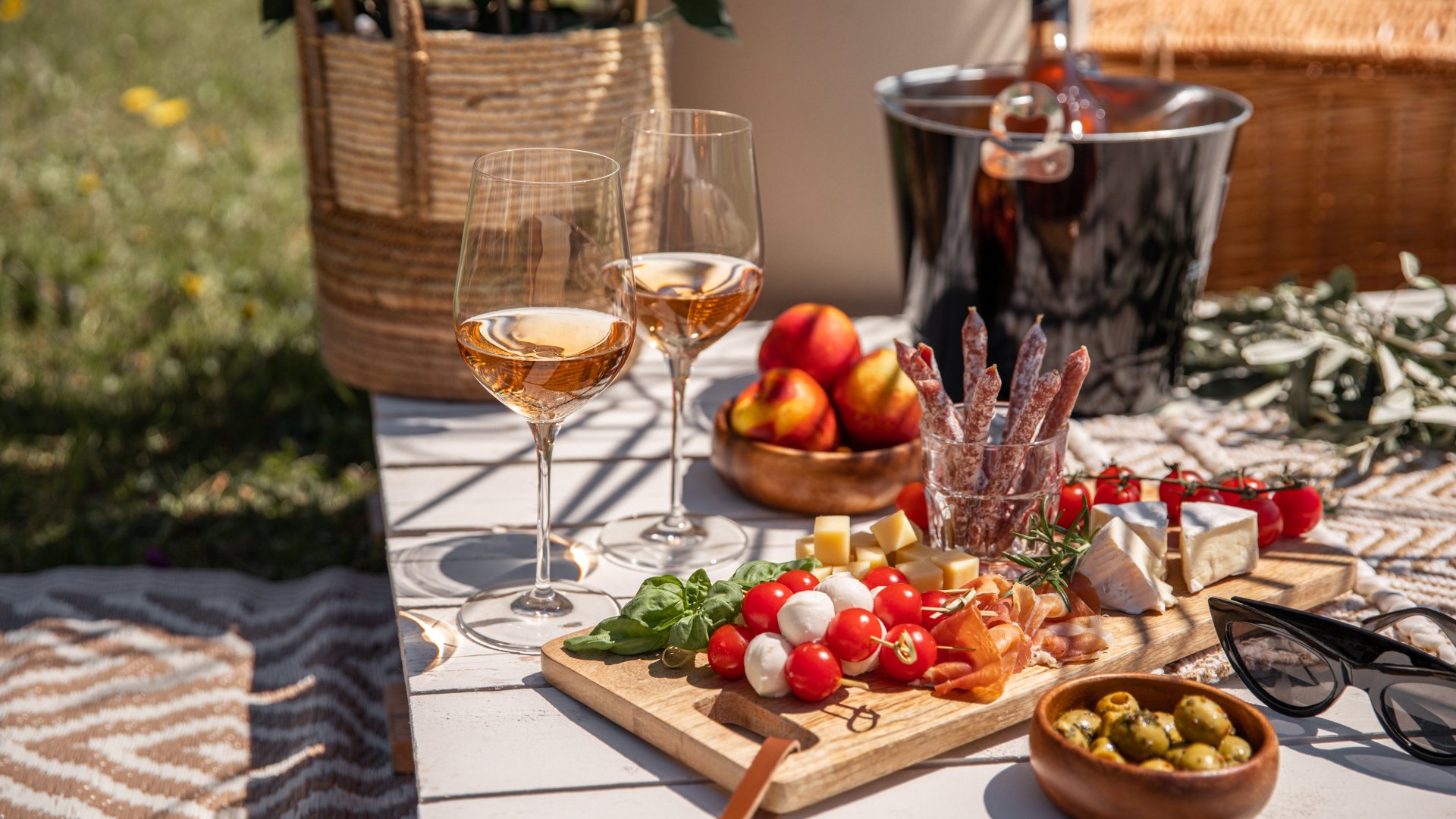 Rose wine glasses with antipasti picnic food snacks on sunny garden party table