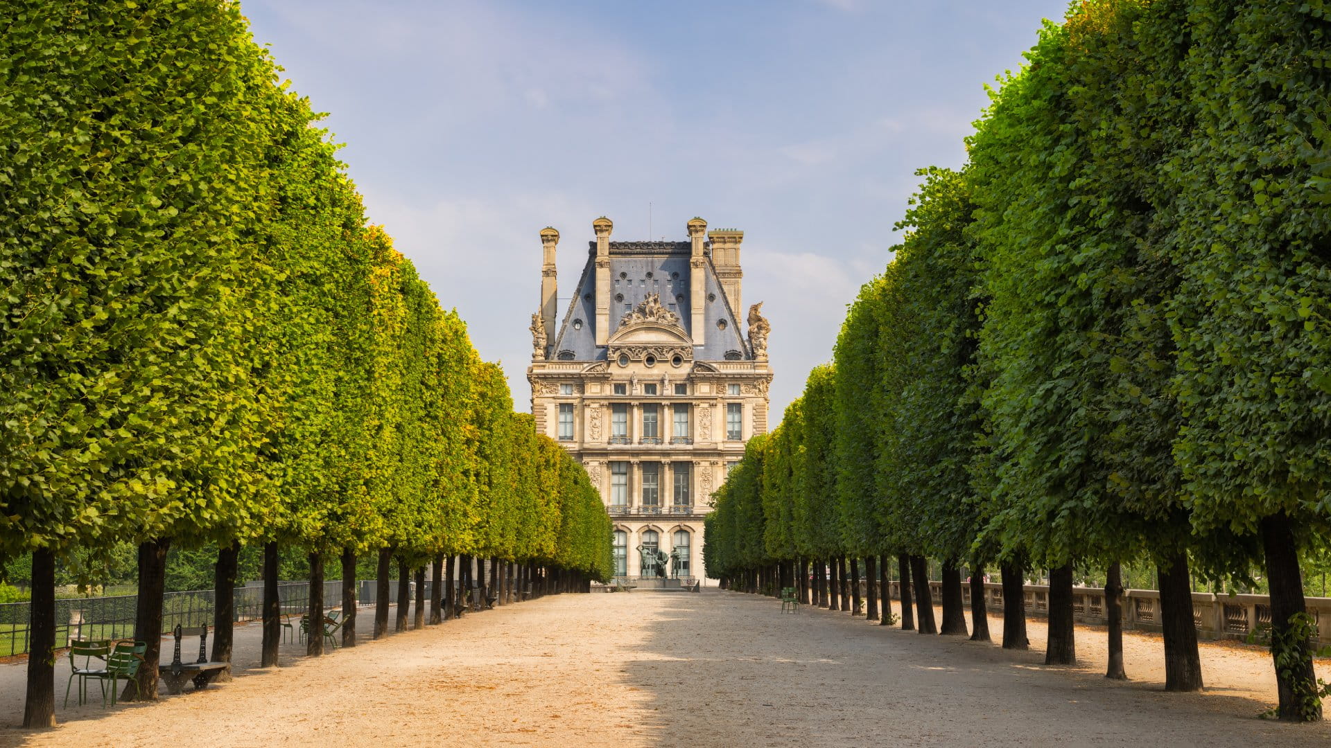 Summer morning view of Tuilleries garden in Paris, France. Tree-lined path leads to the south west facade of the Louvre Museum.