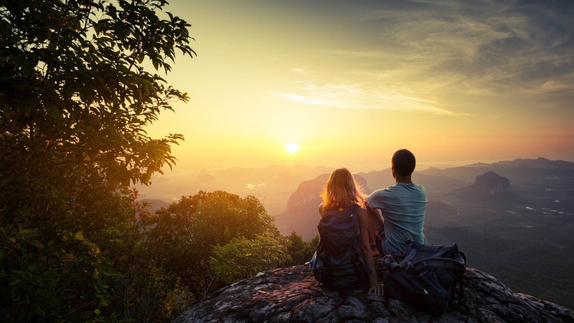 Two hikers on top of the mountain enjoying sunrise over the tropical valley