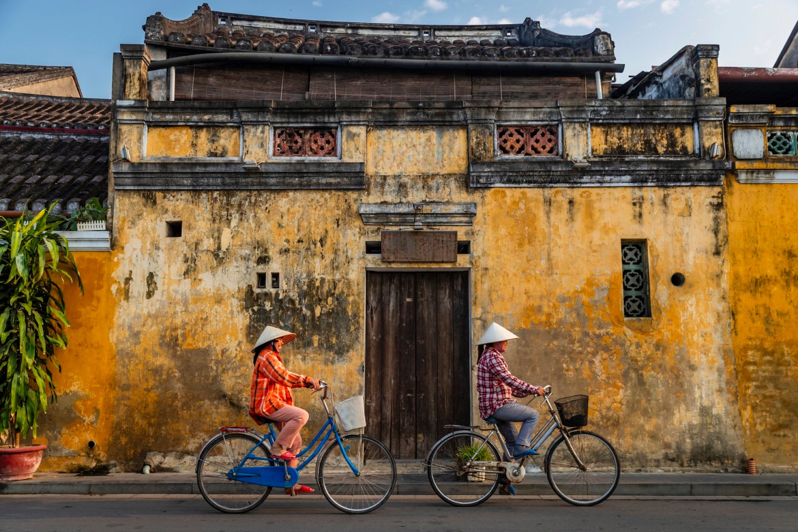 Two women riding bicycles wearing traditional Vietnam clothing in the old town of Hoi An in Vietnam