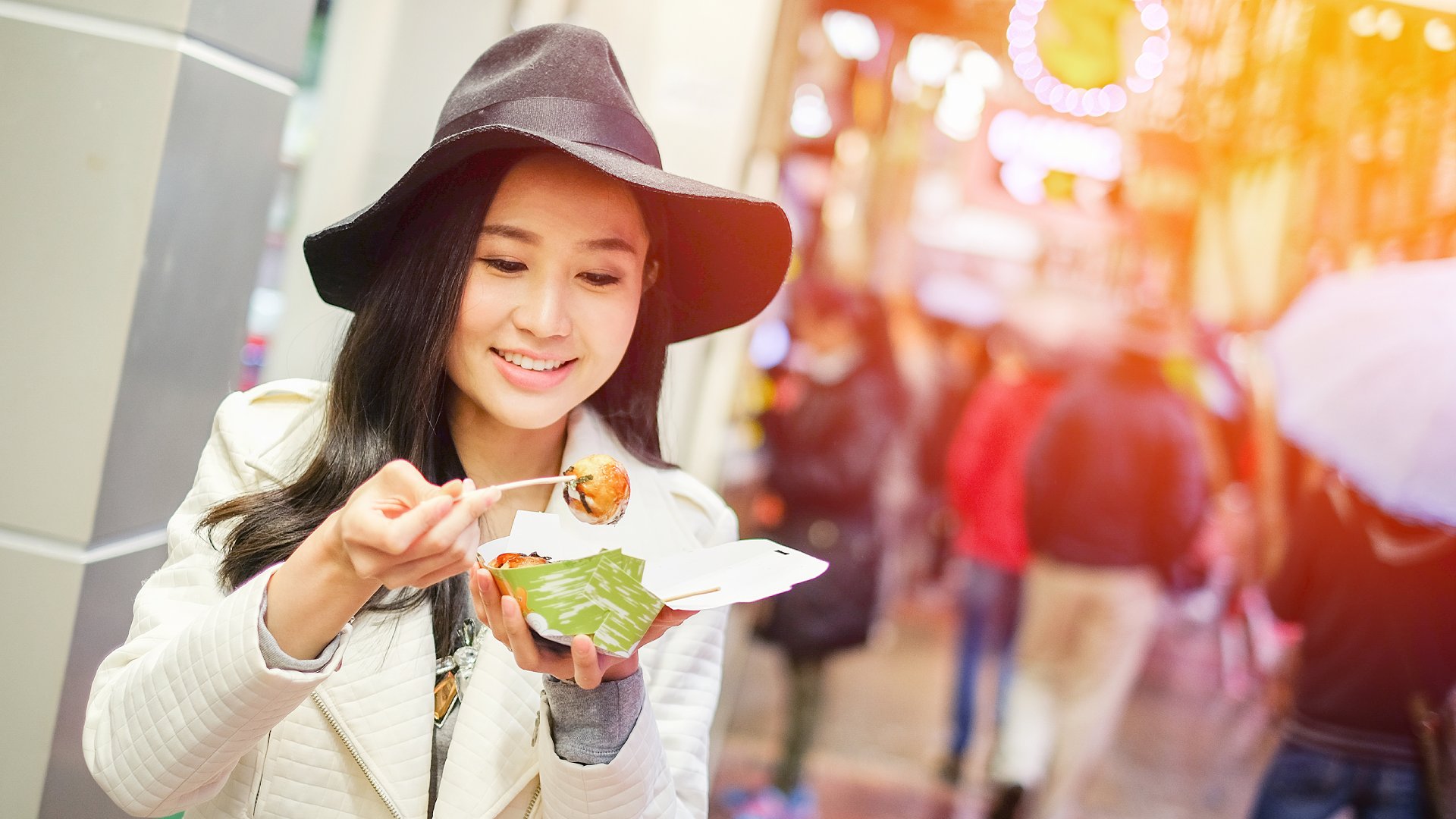 Young Asian Woman Eating Dumpling Batter (Takoyaki) on Street in Hong Kong