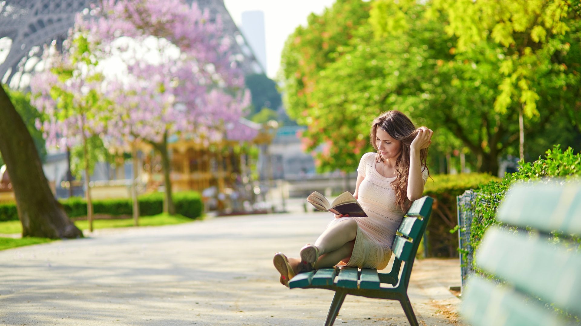 Young woman near the Eiffel Tower, reading on a bench, Paris, France