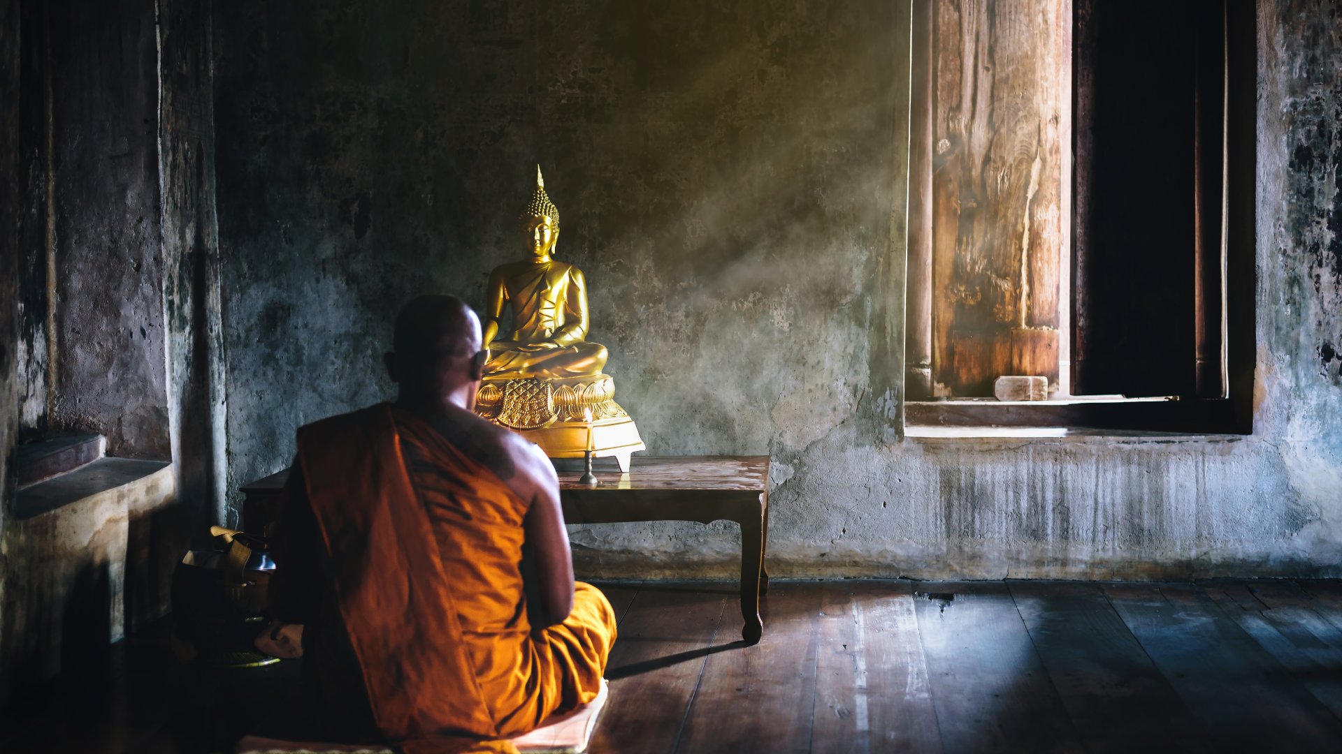 a Buddhist monk meditates in front of a statue of the Buddha in Thailand